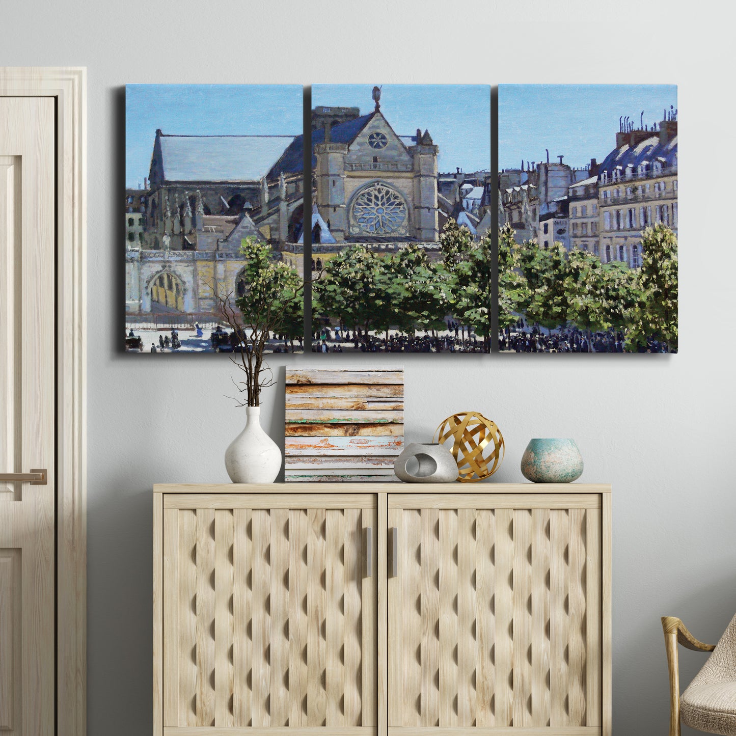Three-panel canvas wall art featuring gothic church within city setting, displayed above a cabinet in an entryway.