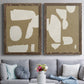 Set of two walnut barnwood framed canvas prints depicting paired bold minimalist shape abstracts with flat blocky forms, rough painted edges, and strong negative space above a sofa in a contemporary living room.