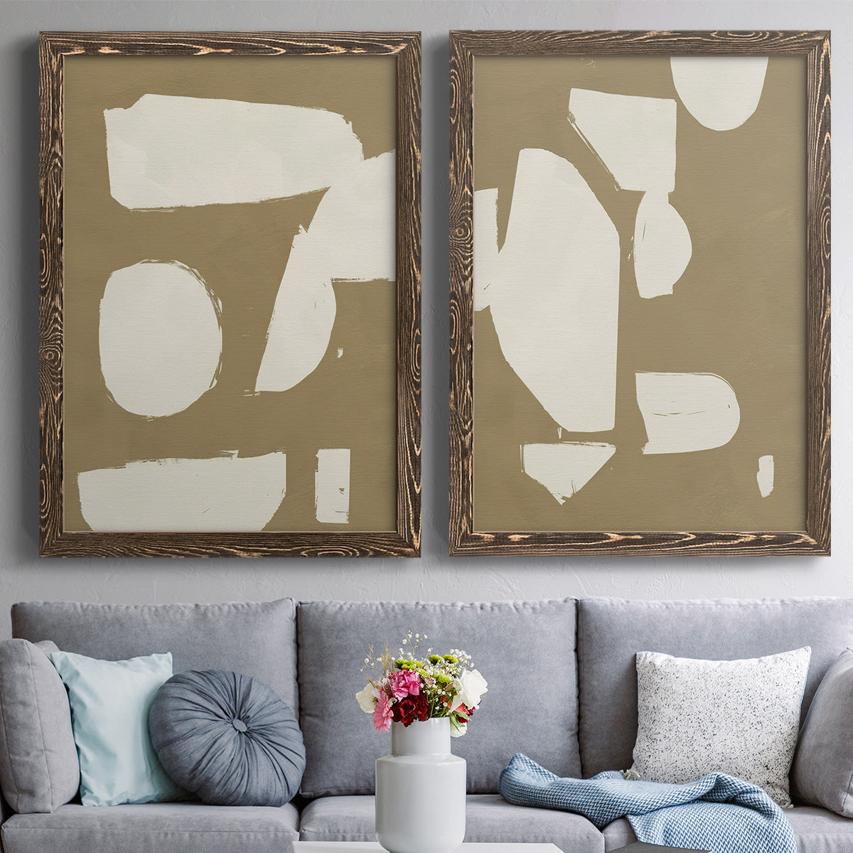 Set of two walnut barnwood framed canvas prints depicting paired bold minimalist shape abstracts with flat blocky forms, rough painted edges, and strong negative space above a sofa in a contemporary living room.