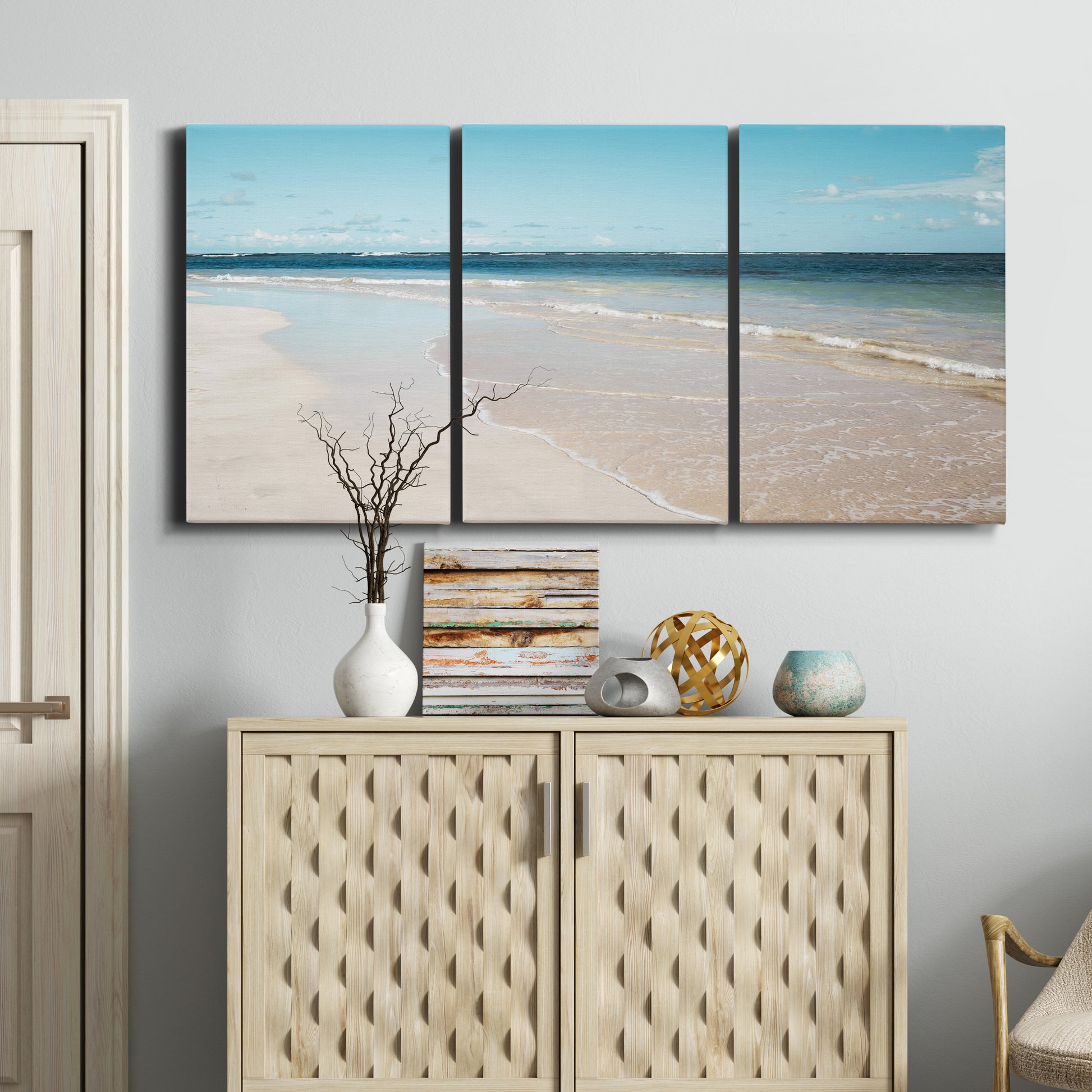 Three-panel canvas wall art featuring white sand beach with gentle waves, displayed above a cabinet in an entryway.