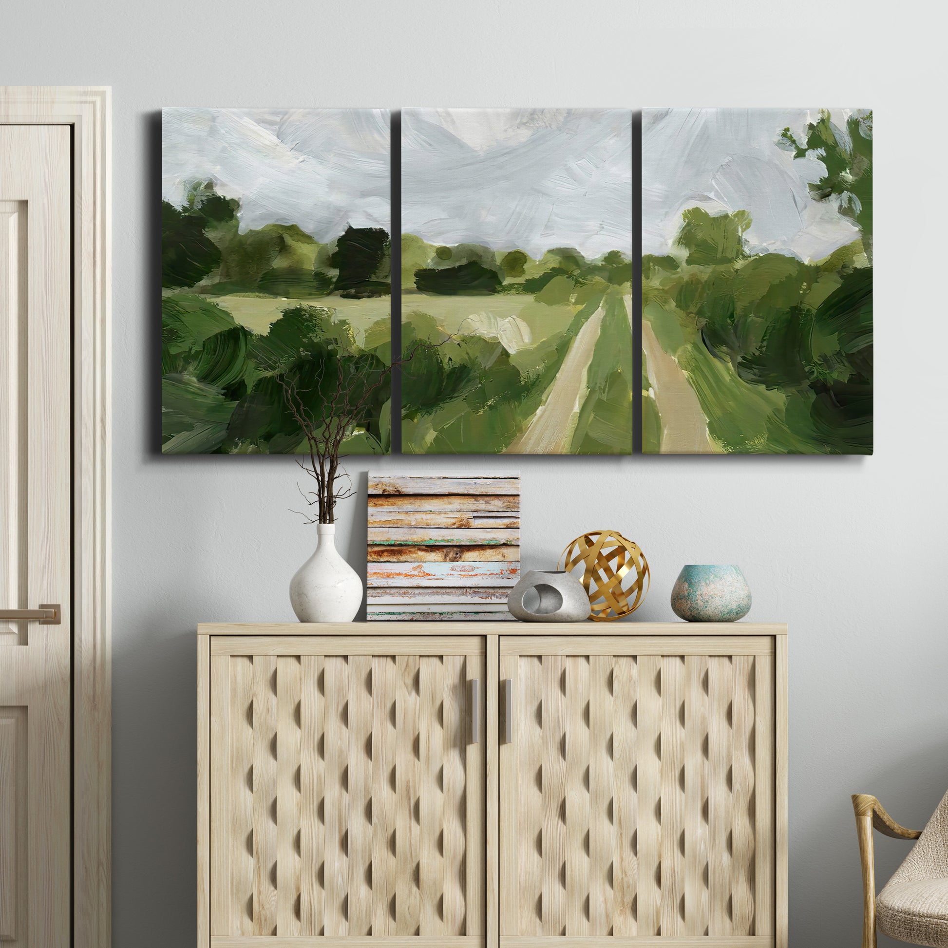 Three-panel canvas wall art featuring meadow trail through open grassland, displayed above a cabinet in an entryway.