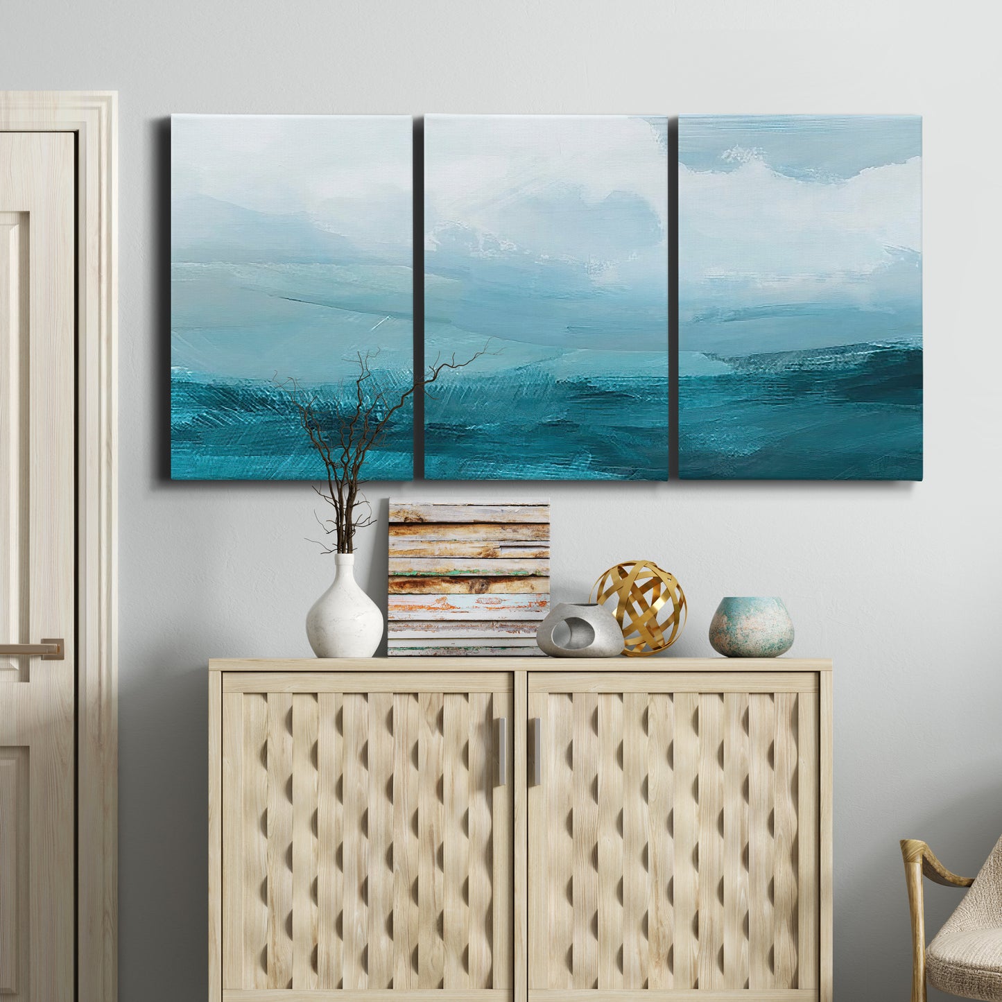 Three-panel canvas wall art featuring vertical coastal elements with rising light, displayed above a cabinet in an entryway.