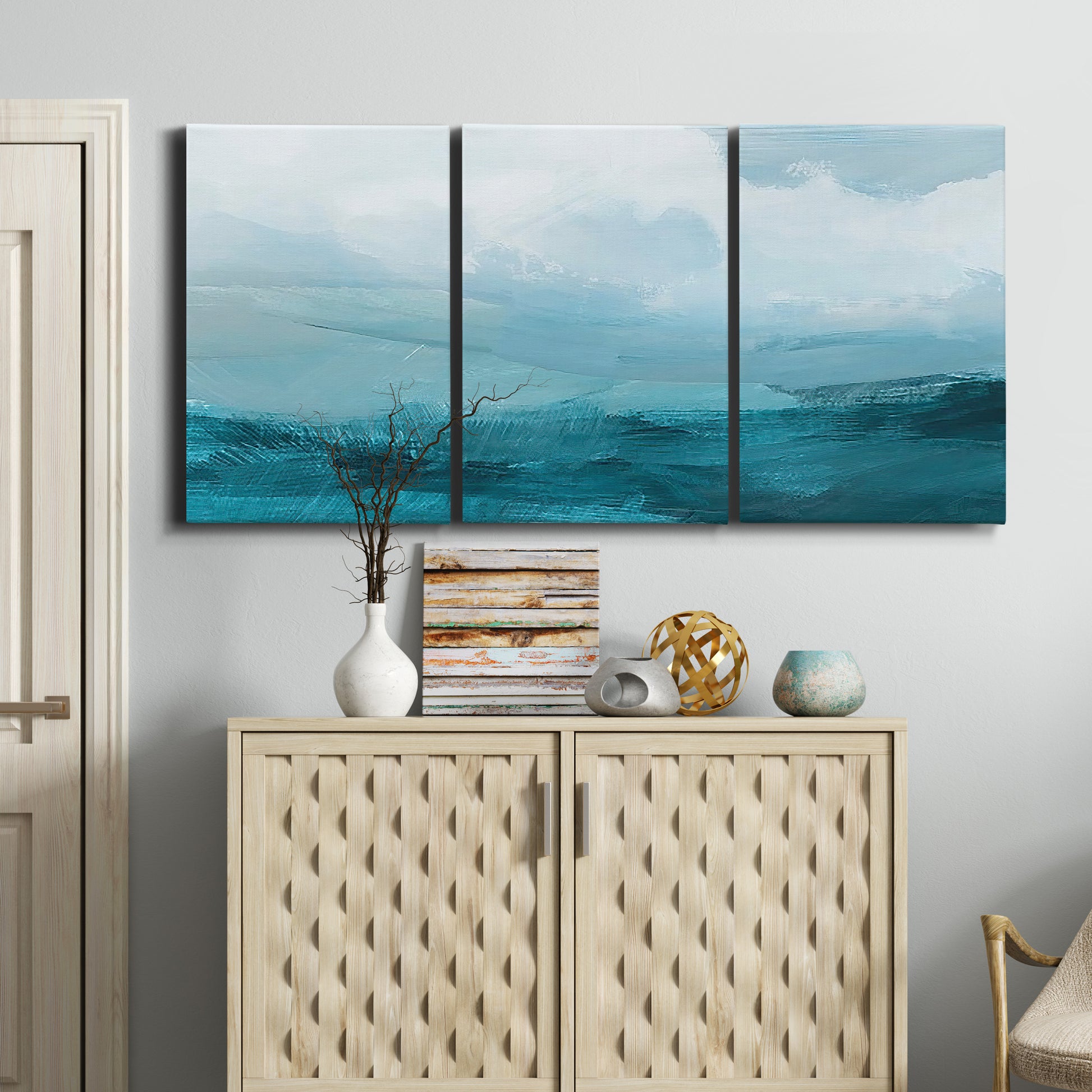 Three-panel canvas wall art featuring vertical coastal elements with rising light, displayed above a cabinet in an entryway.