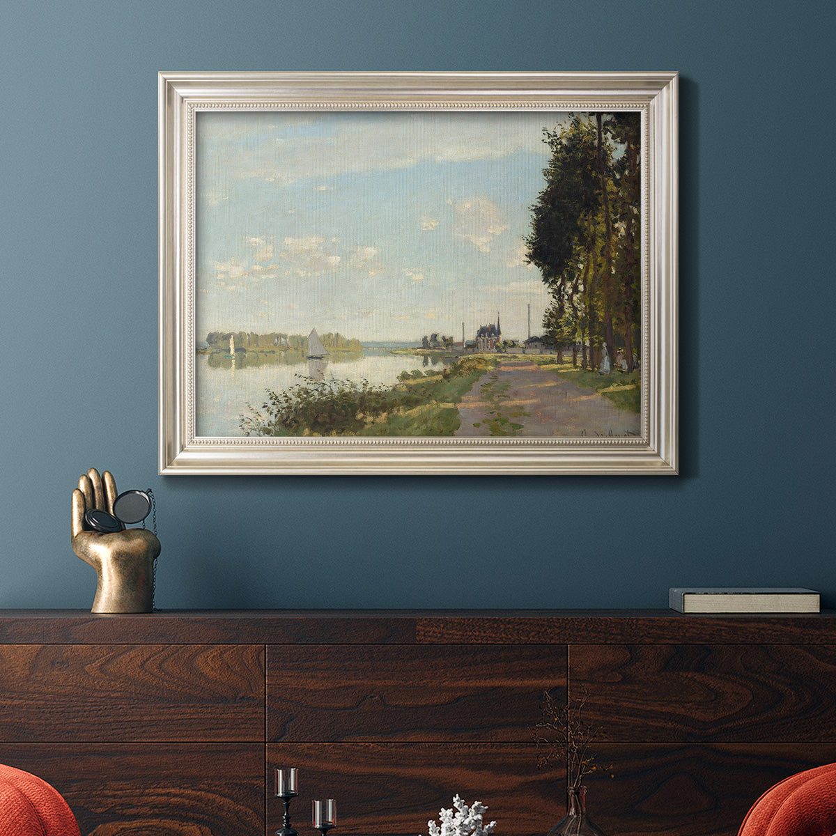 Impressionist river scene with red boats by Claude Monet in an ornate champagne frame displayed in a dark-toned interior setting.