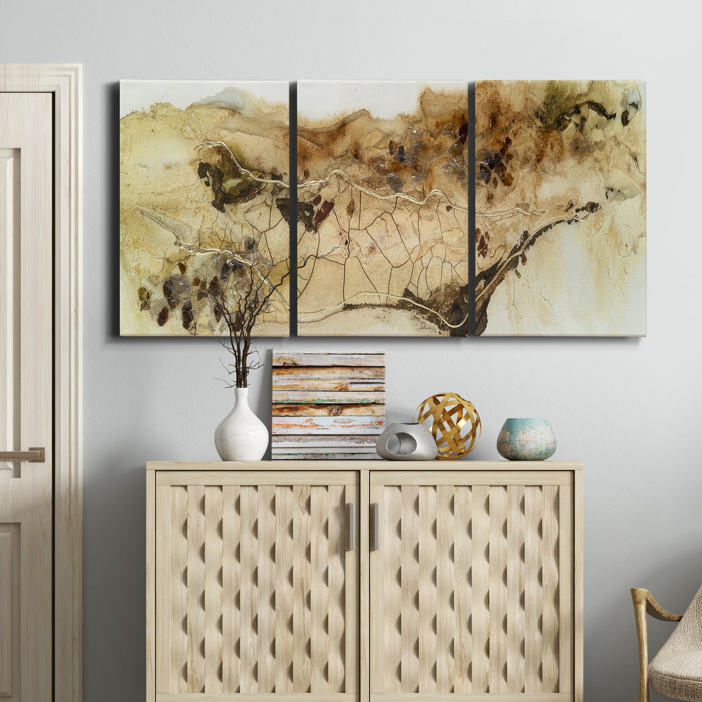 Three-panel canvas wall art featuring muted abstract with metallic gold accents, displayed above a cabinet in an entryway.