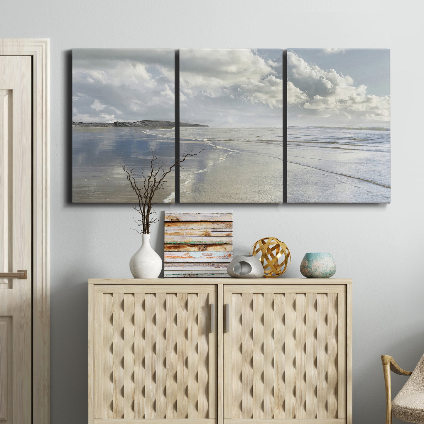 Three-panel canvas wall art featuring endless beach meeting ocean horizon, displayed above a cabinet in an entryway.