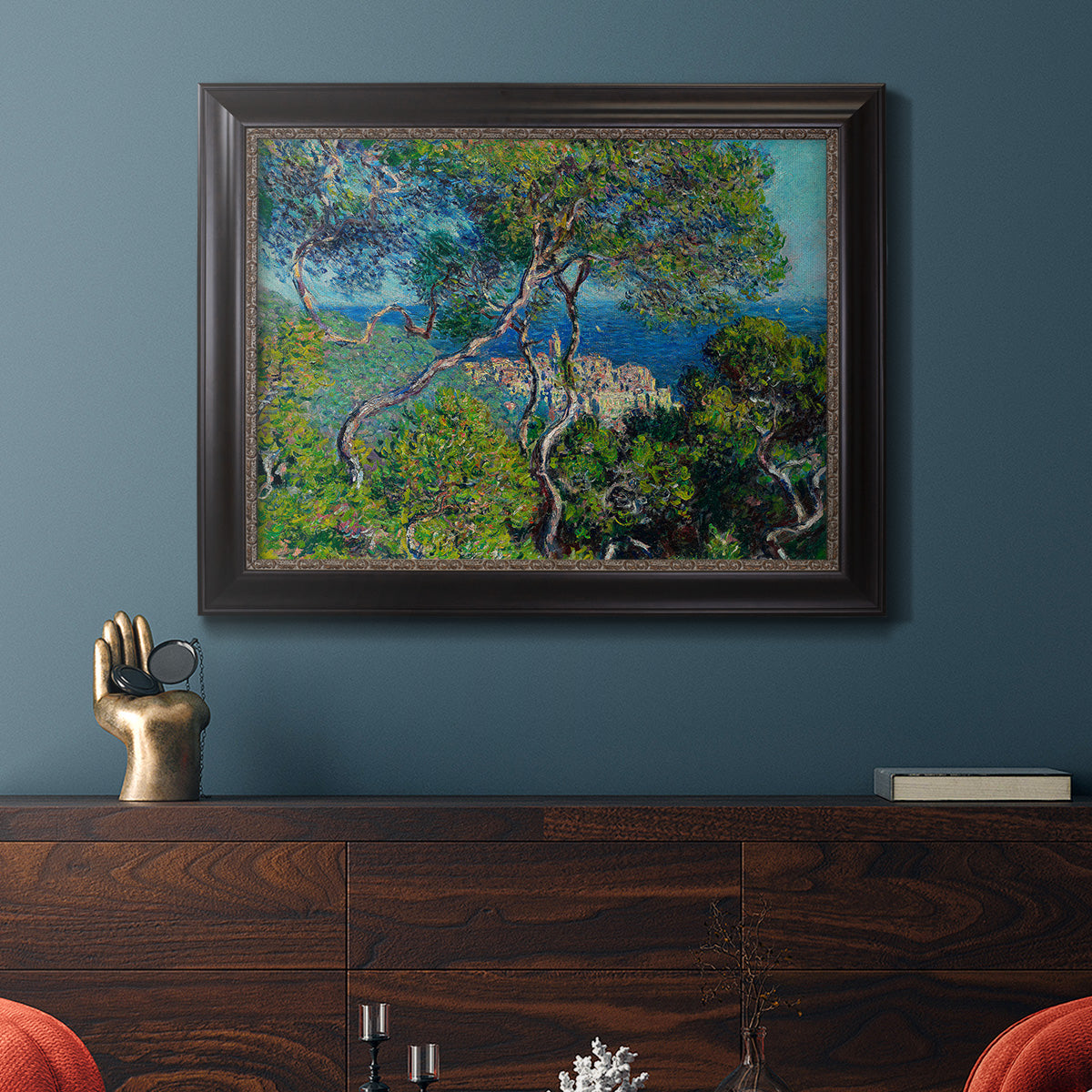 Impressionist Mediterranean coastal landscape by Claude Monet in an ornate black frame with gilded inner detail displayed in a dark-toned interior setting.