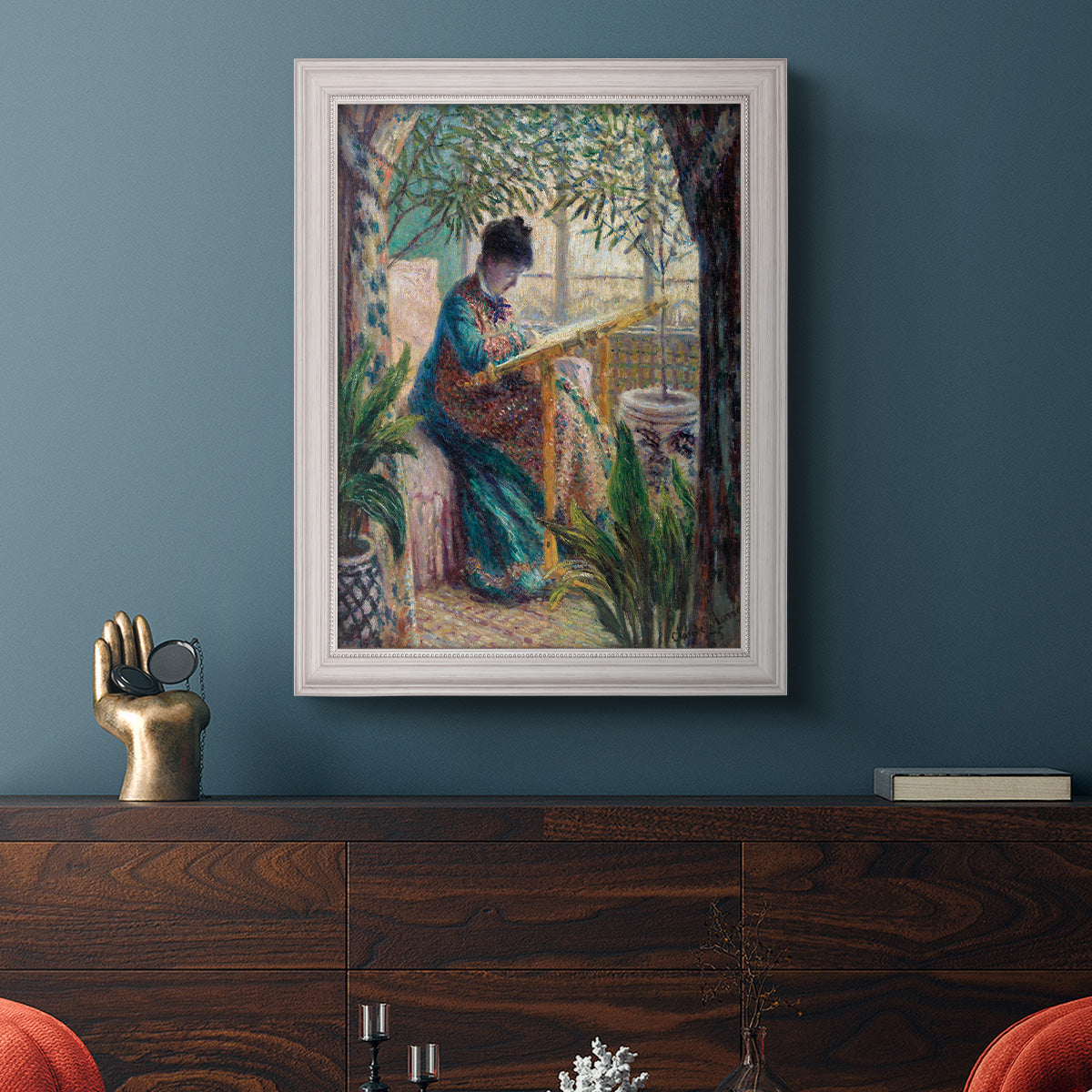 Impressionist portrait of Madame Monet sewing by Claude Monet in an ornate weathered white frame displayed in a dark-toned interior setting.