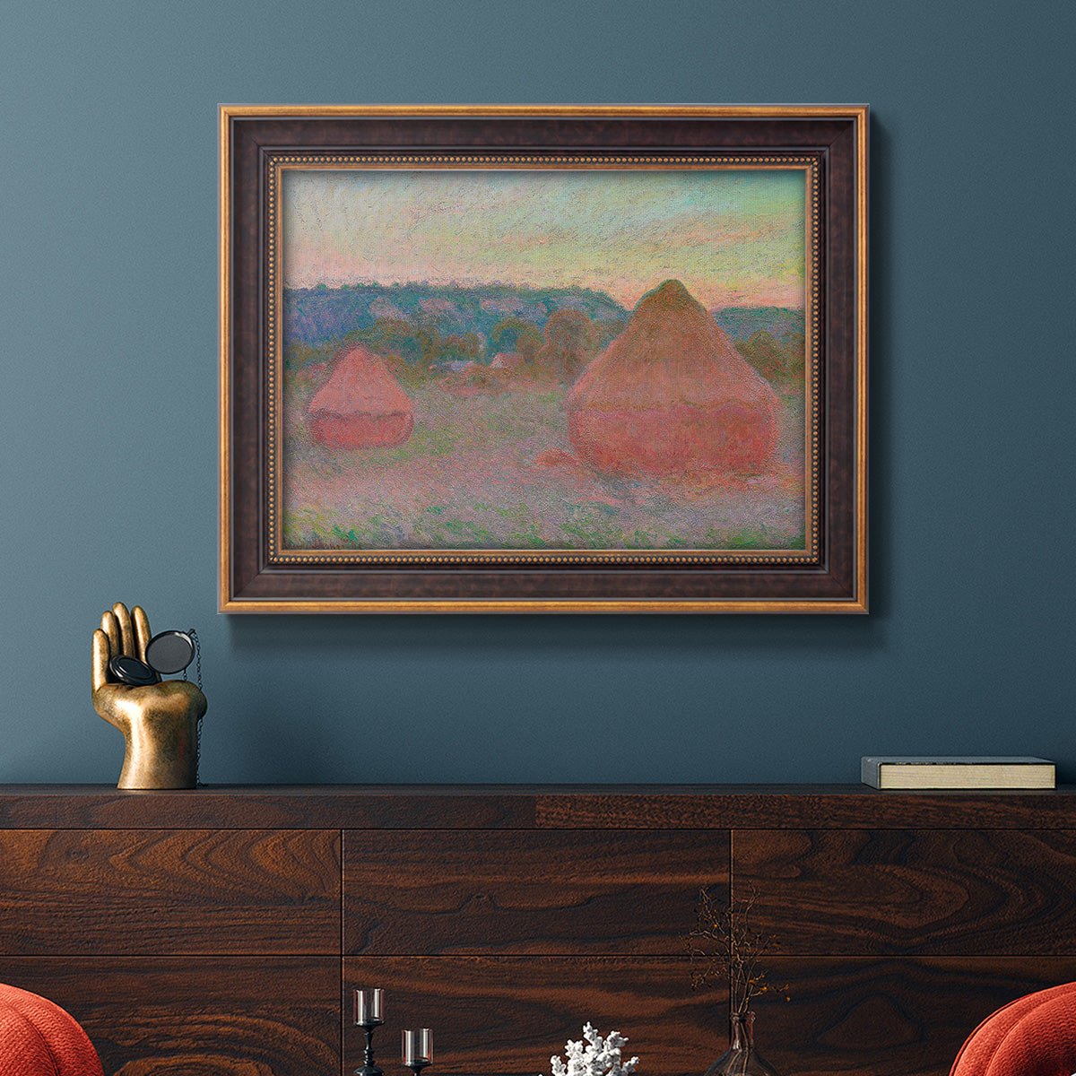 Impressionist haystack series landscape by Claude Monet in an ornate bronzed mahogany wood frame displayed in a dark-toned interior setting.