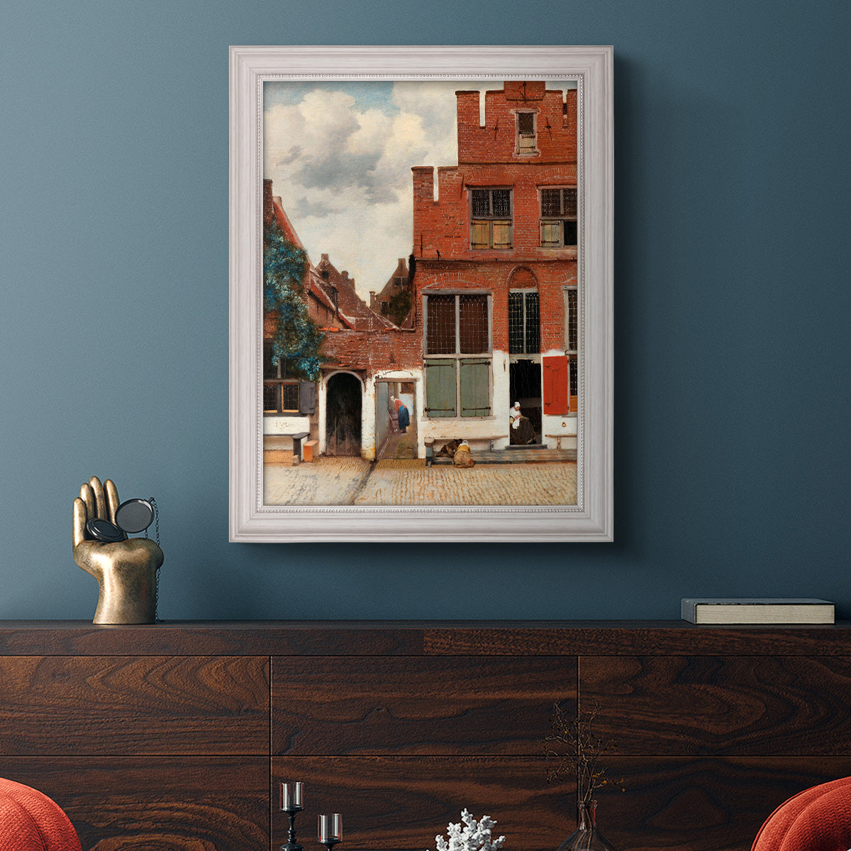 Realist city street scene by Johannes Vermeer in an ornate weathered white frame displayed in a dark-toned interior setting.
