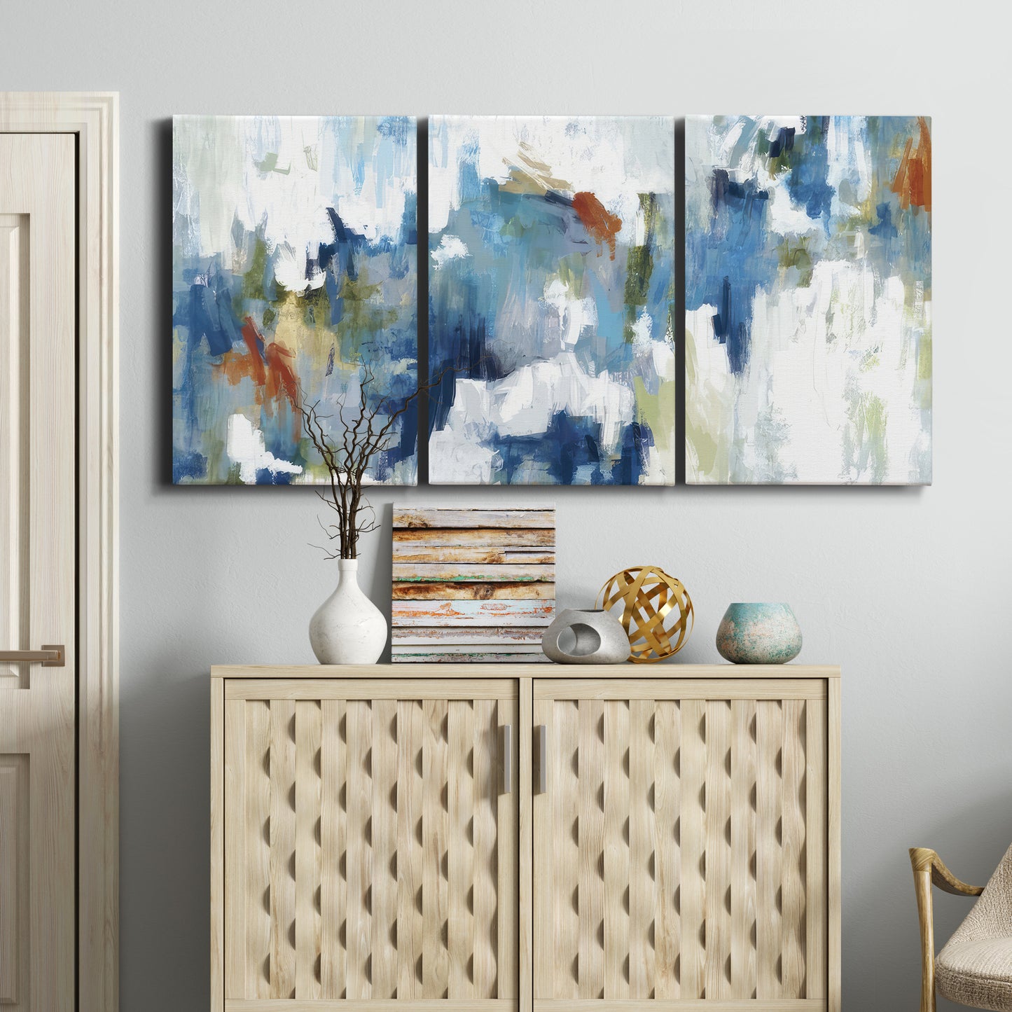 Three-panel canvas wall art featuring flowing abstract color movement, displayed above a cabinet in an entryway.