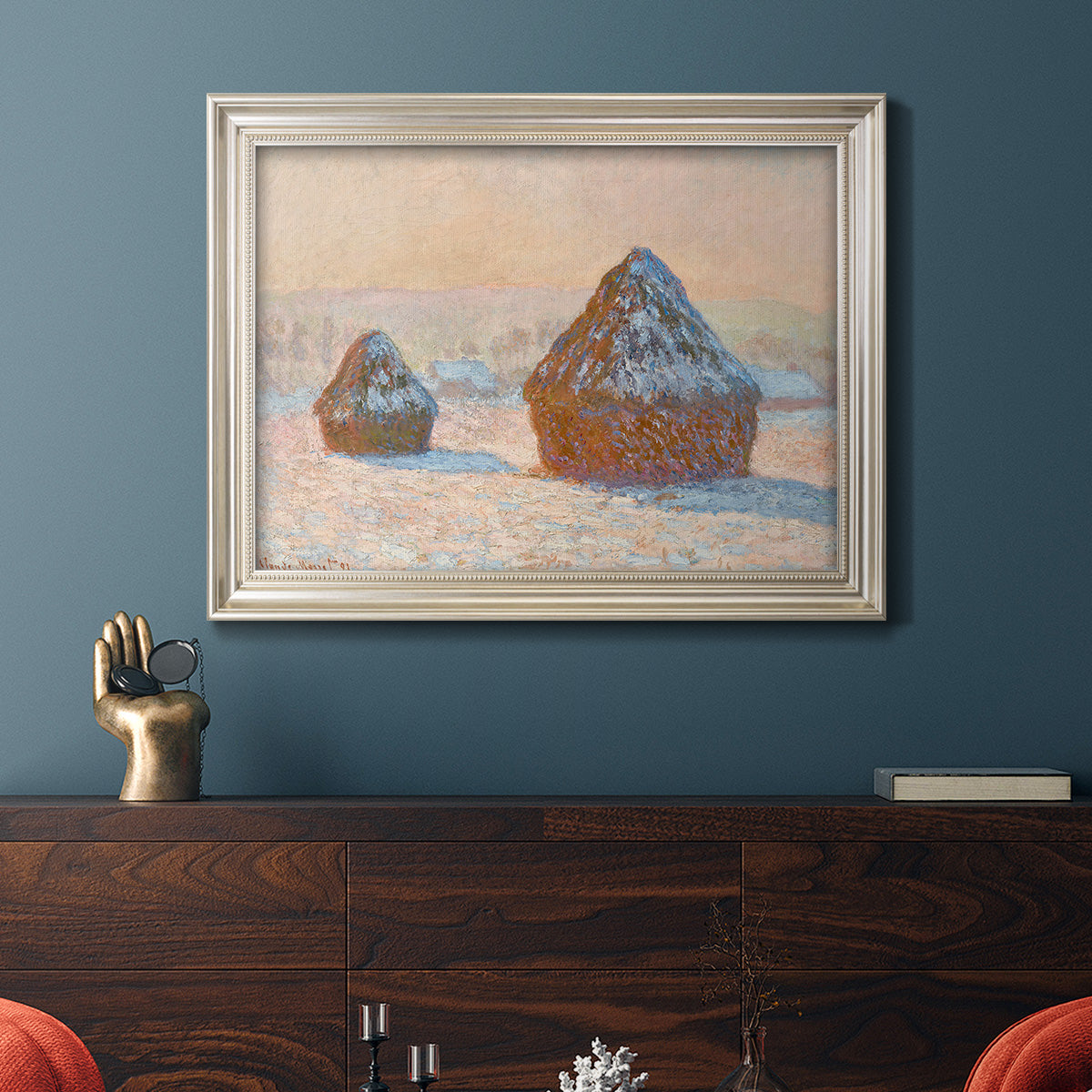 Impressionist winter haystack scene by Claude Monet in an ornate champagne frame displayed in a dark-toned interior setting.