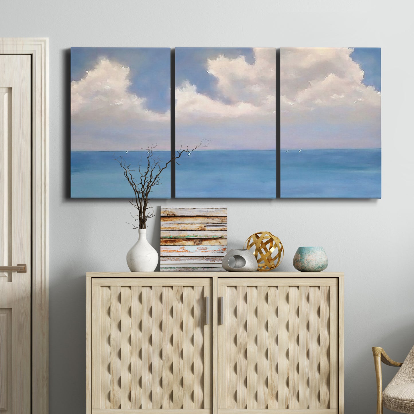 Three-panel canvas wall art featuring coastal shoreline with distant horizon, displayed above a cabinet in an entryway.