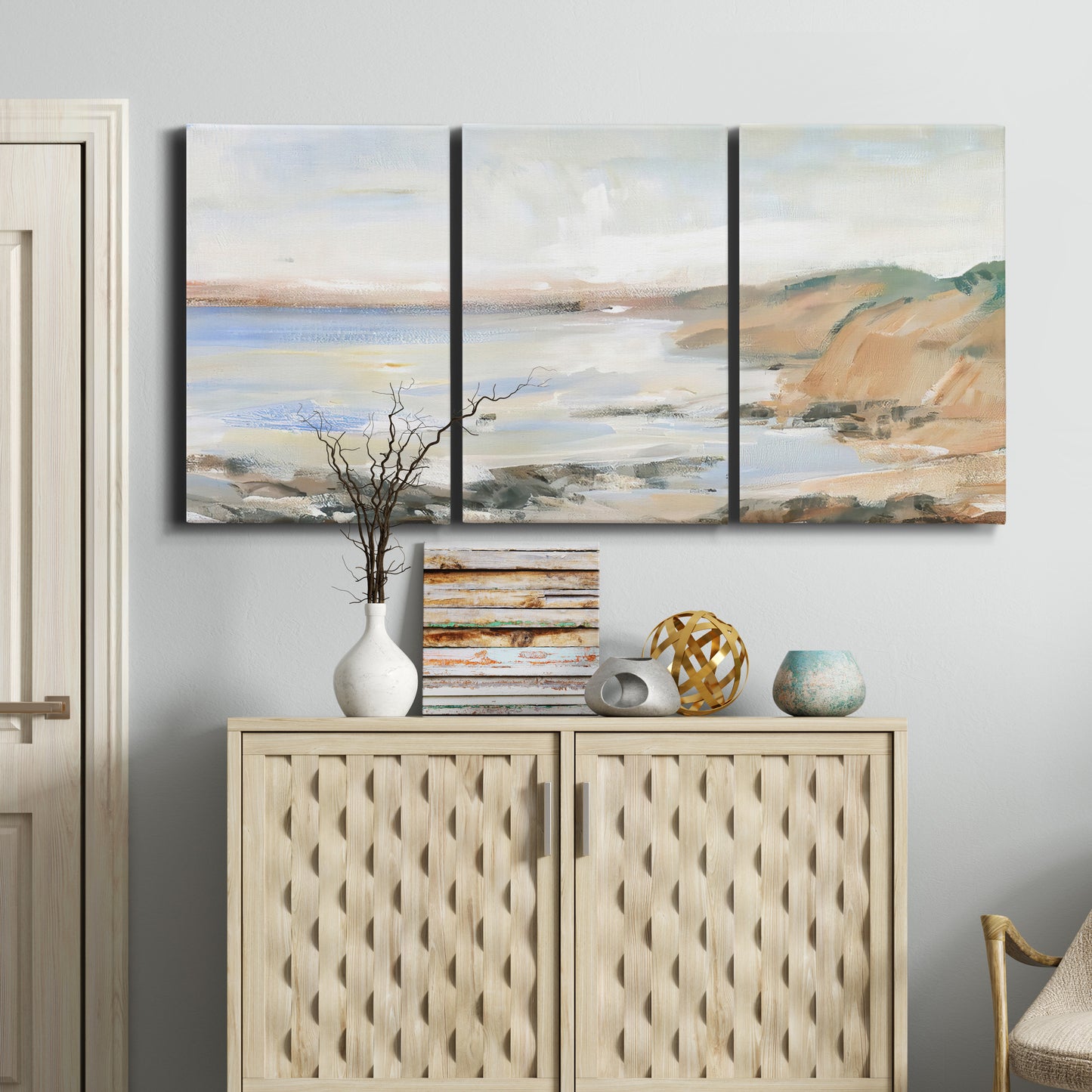 Three-panel canvas wall art featuring coastal shoreline landscape study, displayed above a cabinet in an entryway.