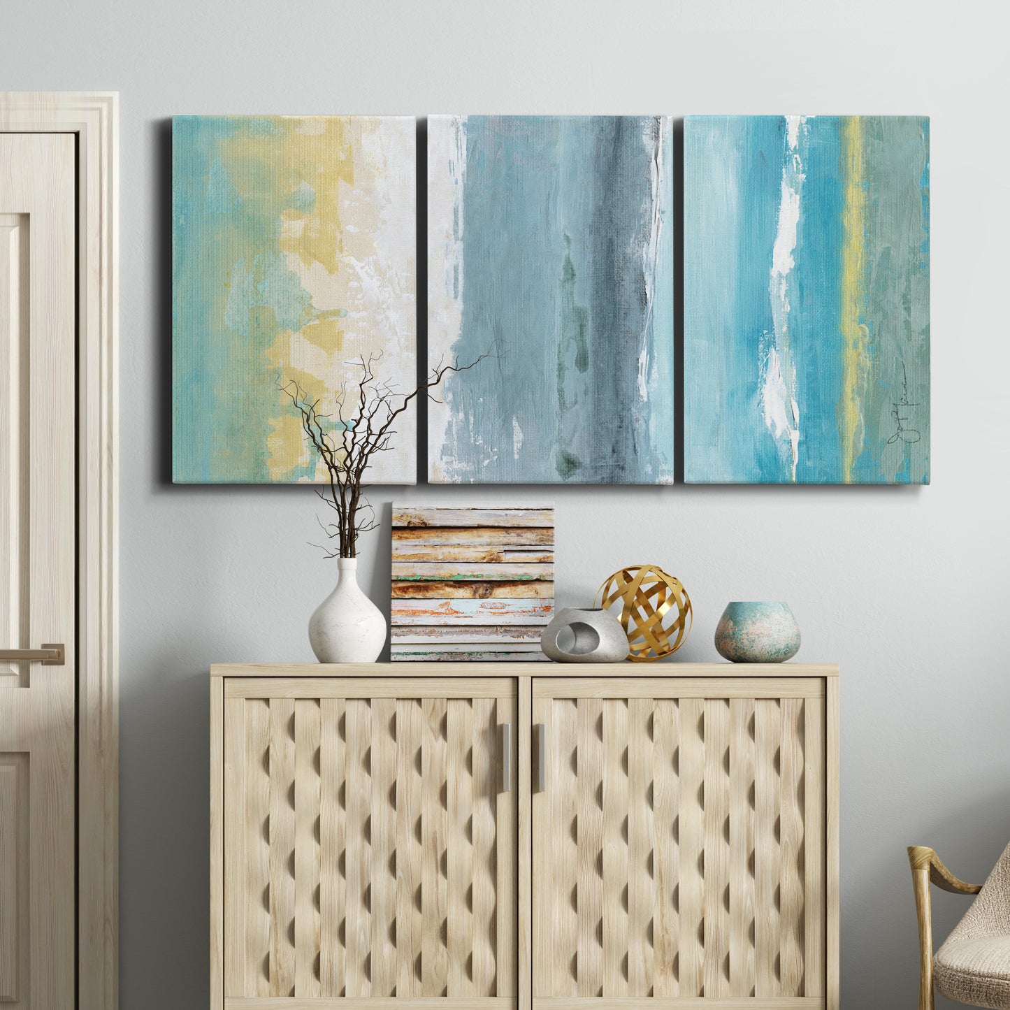 Three-panel canvas wall art featuring abstract coastal beach textures, displayed above a cabinet in an entryway.