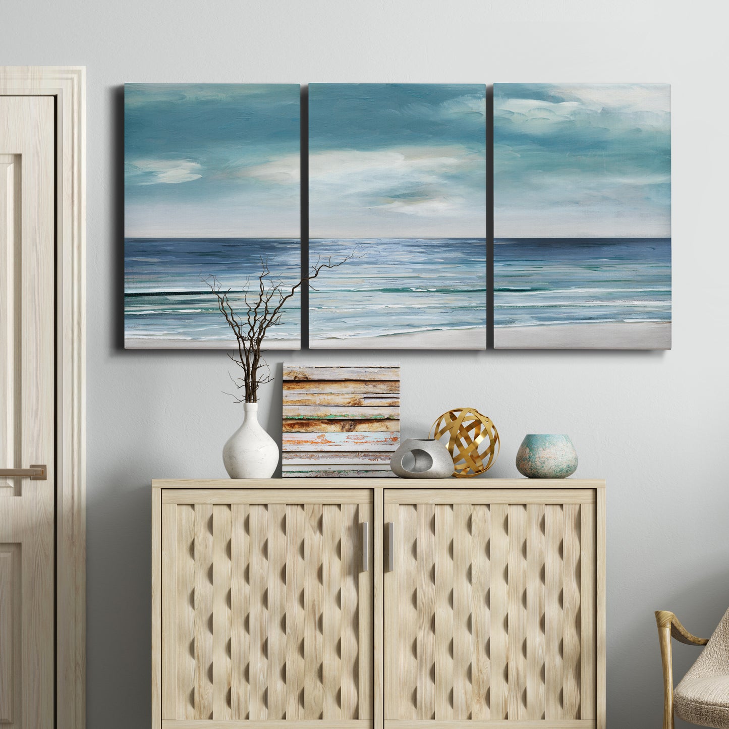 Three-panel canvas wall art featuring calm coastal shoreline, displayed above a cabinet in an entryway.
