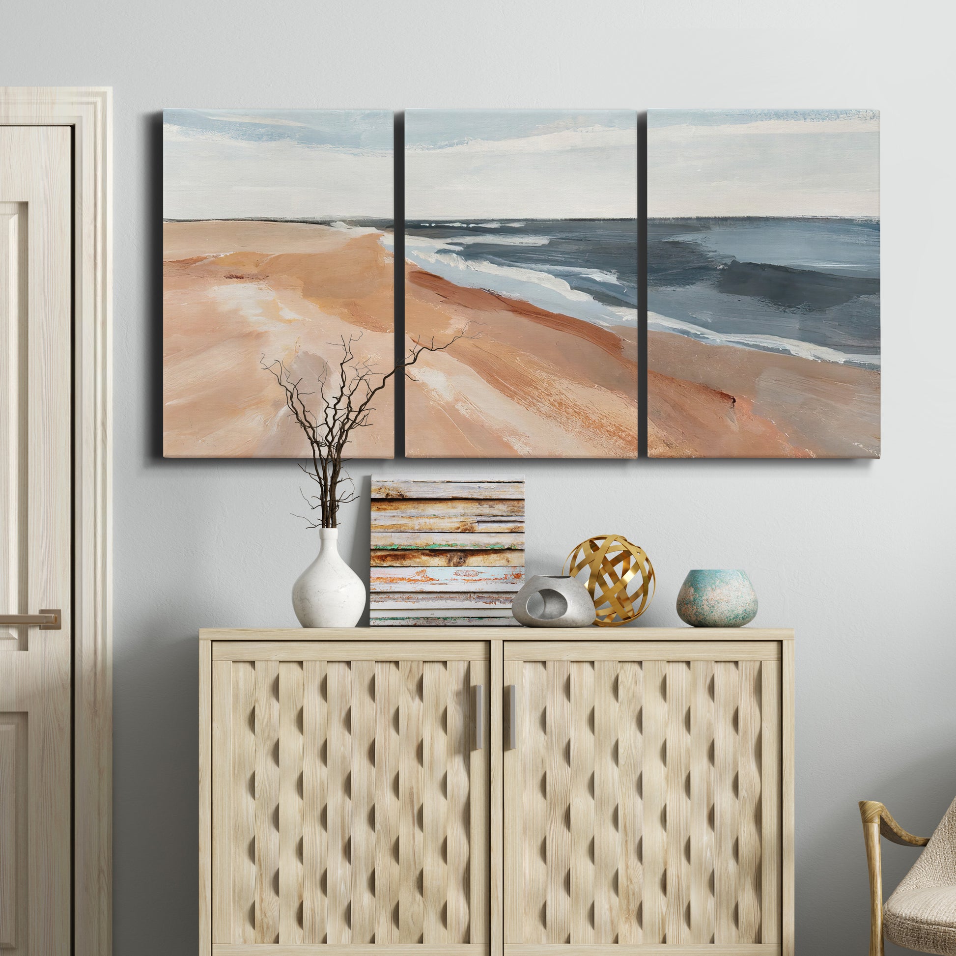 Three-panel canvas wall art featuring abstract coastal beach composition, displayed above a cabinet in an entryway.