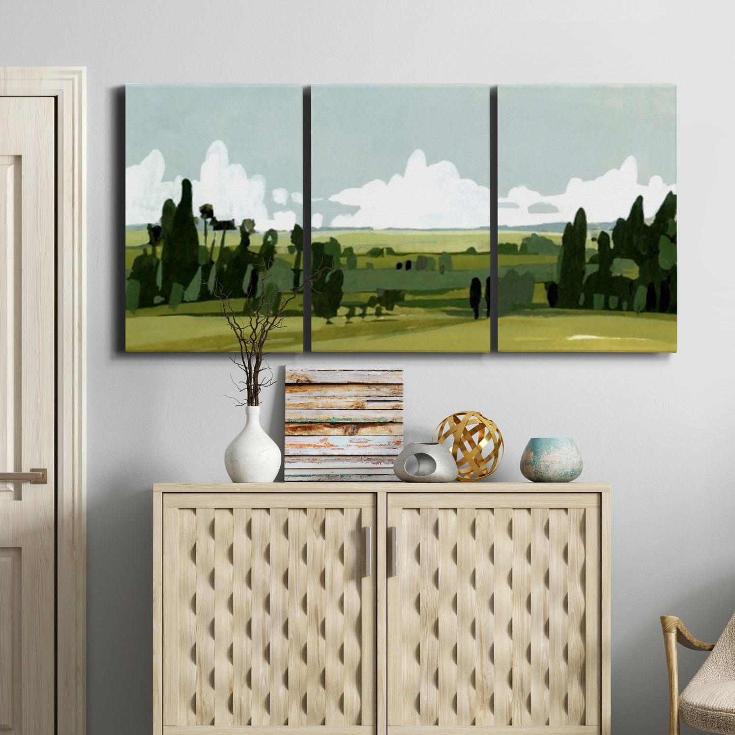 Three-panel canvas wall art featuring lush green summer countryside, displayed above a cabinet in an entryway.