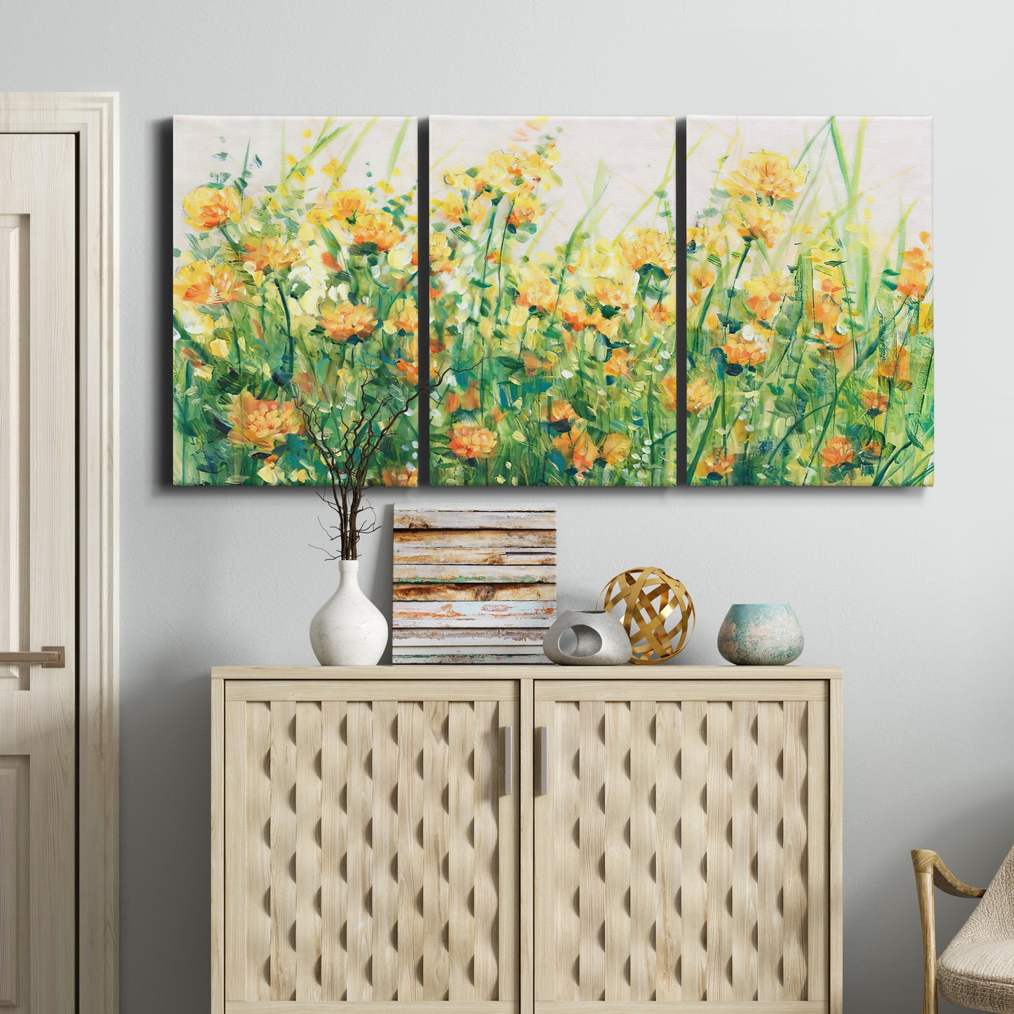 Three-panel canvas wall art featuring colorful garden flowers in bloom, displayed above a cabinet in an entryway.