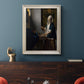 Quiet interior genre scene of a woman with scales by Johannes Vermeer in an ornate champagne frame displayed in a dark-toned interior setting.