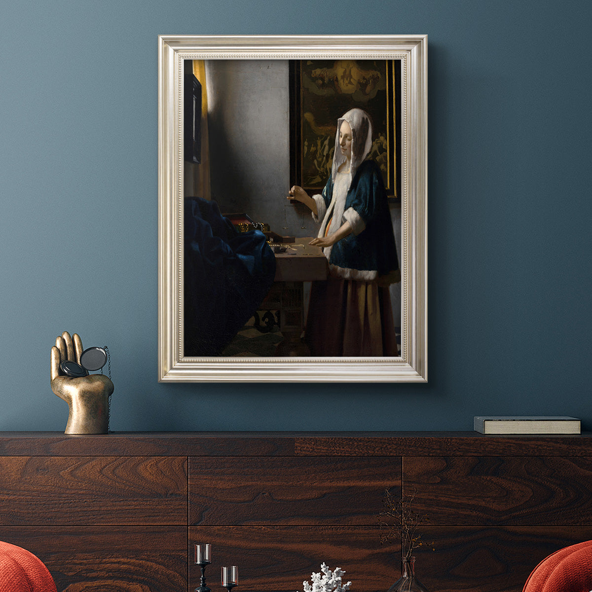 Quiet interior genre scene of a woman with scales by Johannes Vermeer in an ornate champagne frame displayed in a dark-toned interior setting.