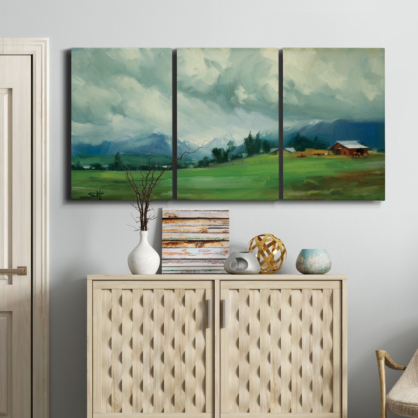 Three-panel canvas wall art featuring wide pastoral valley landscape, displayed above a cabinet in an entryway.