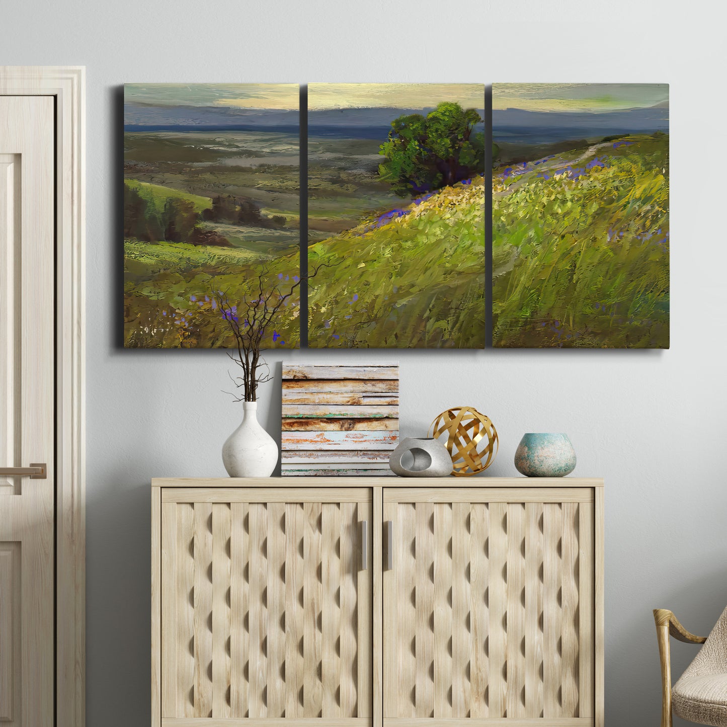 Three-panel canvas wall art featuring winding path through rolling hills, displayed above a cabinet in an entryway.
