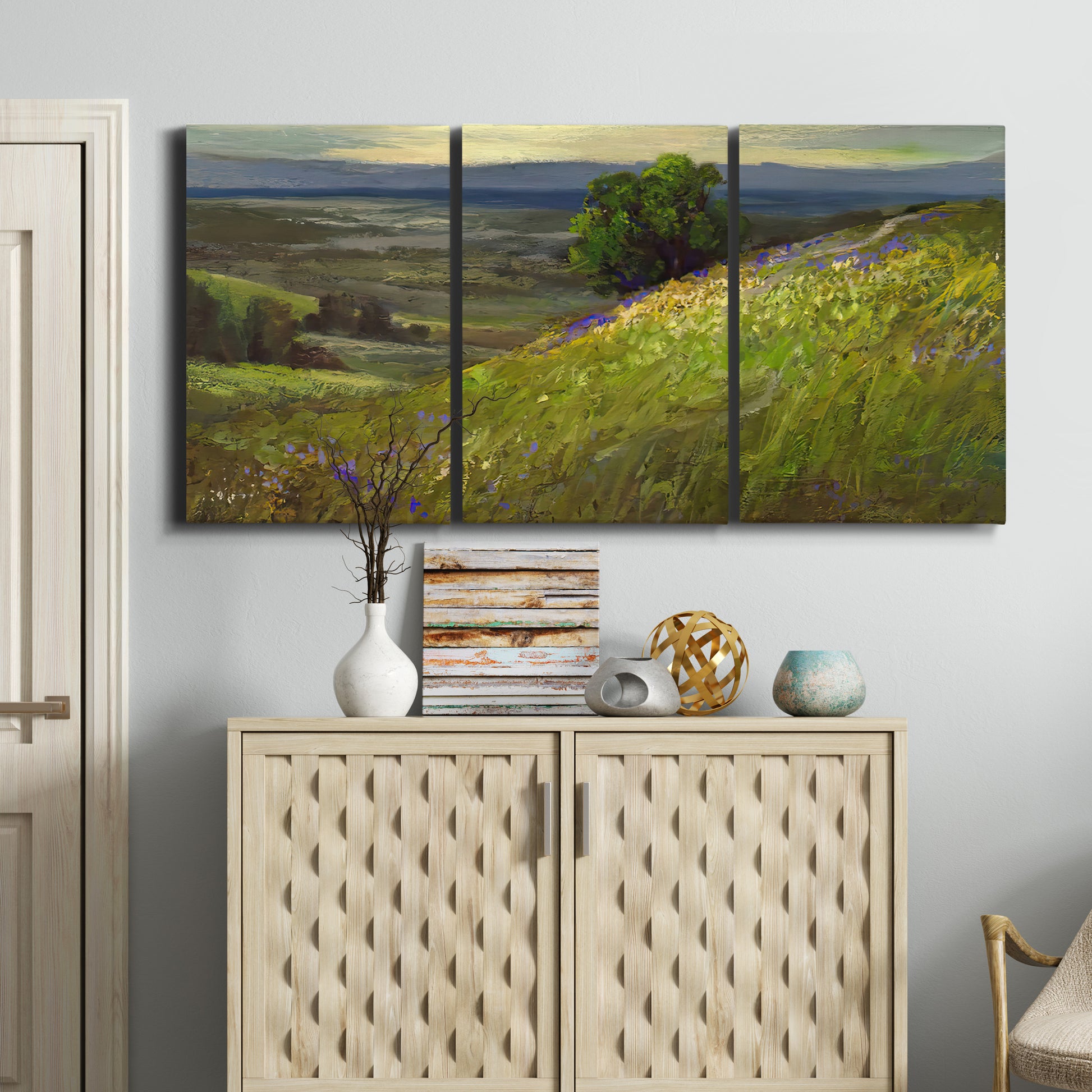 Three-panel canvas wall art featuring winding path through rolling hills, displayed above a cabinet in an entryway.