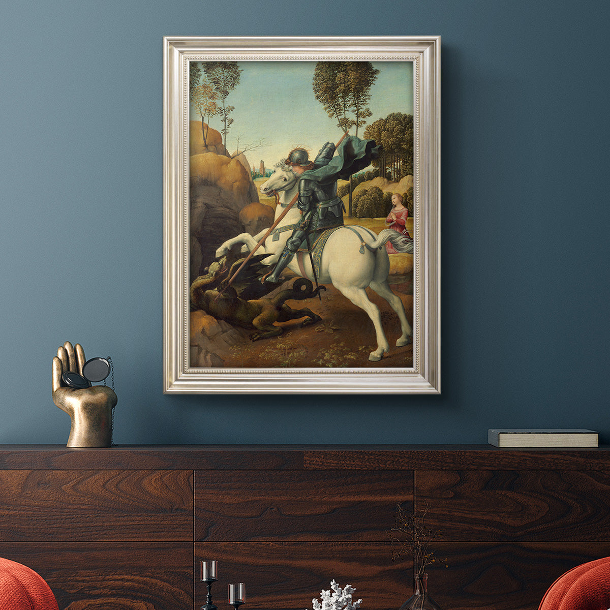 Religious painting of Saint George slaying the dragon by Raphael in an ornate champagne frame displayed in a dark-toned interior setting.