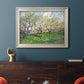Impressionist spring orchard landscape by Vincent van Gogh in an ornate champagne frame displayed in a dark-toned interior setting.