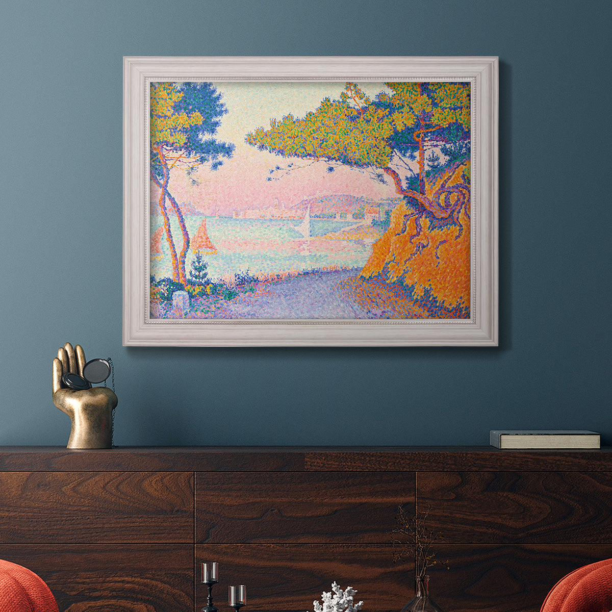 Pointillist coastal seascape by Paul Signac in an ornate weathered white frame displayed in a dark-toned interior setting.