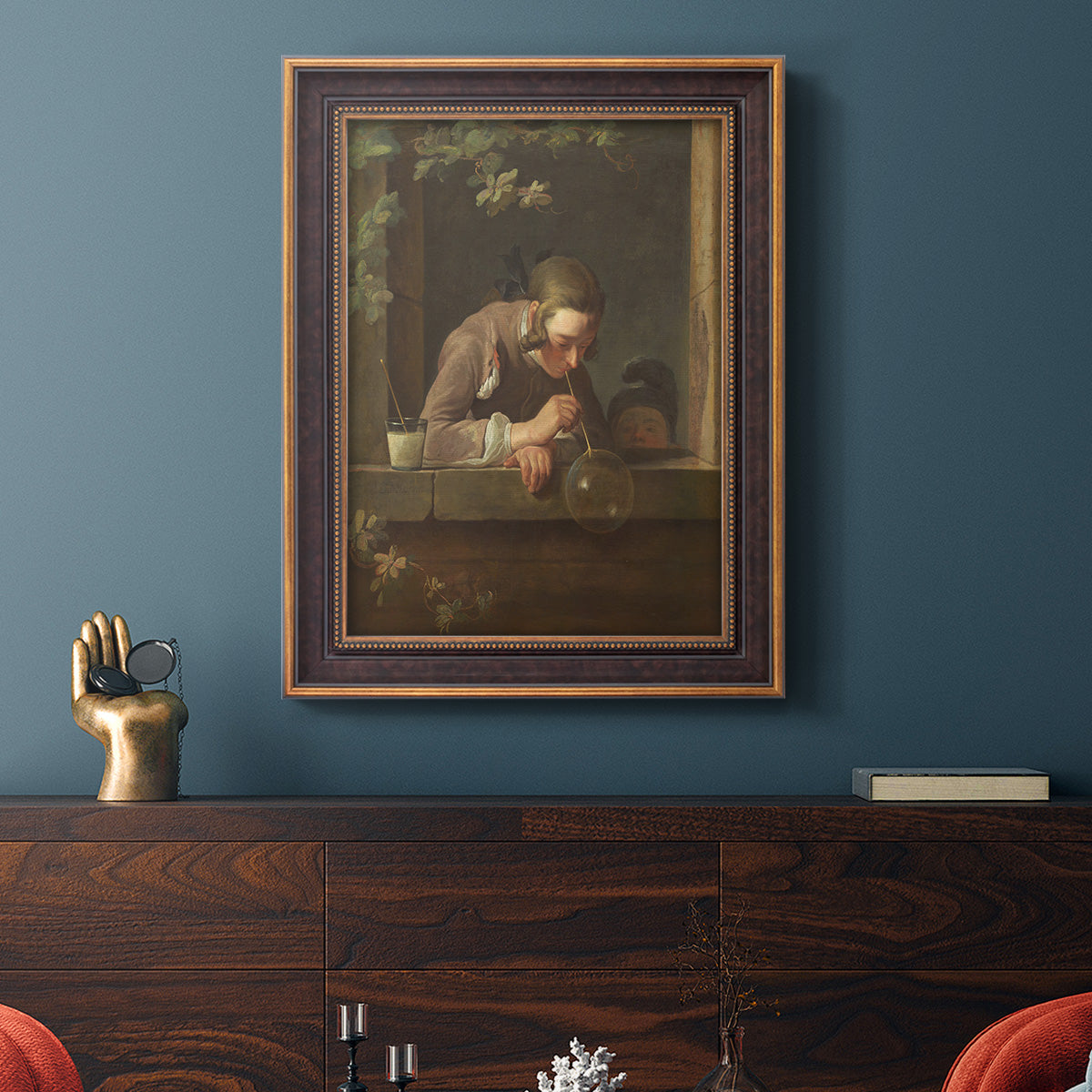 Classical genre painting of a child blowing soap bubbles by Jean-Siméon Chardin in an ornate bronzed mahogany wood frame displayed in a dark-toned interior setting.