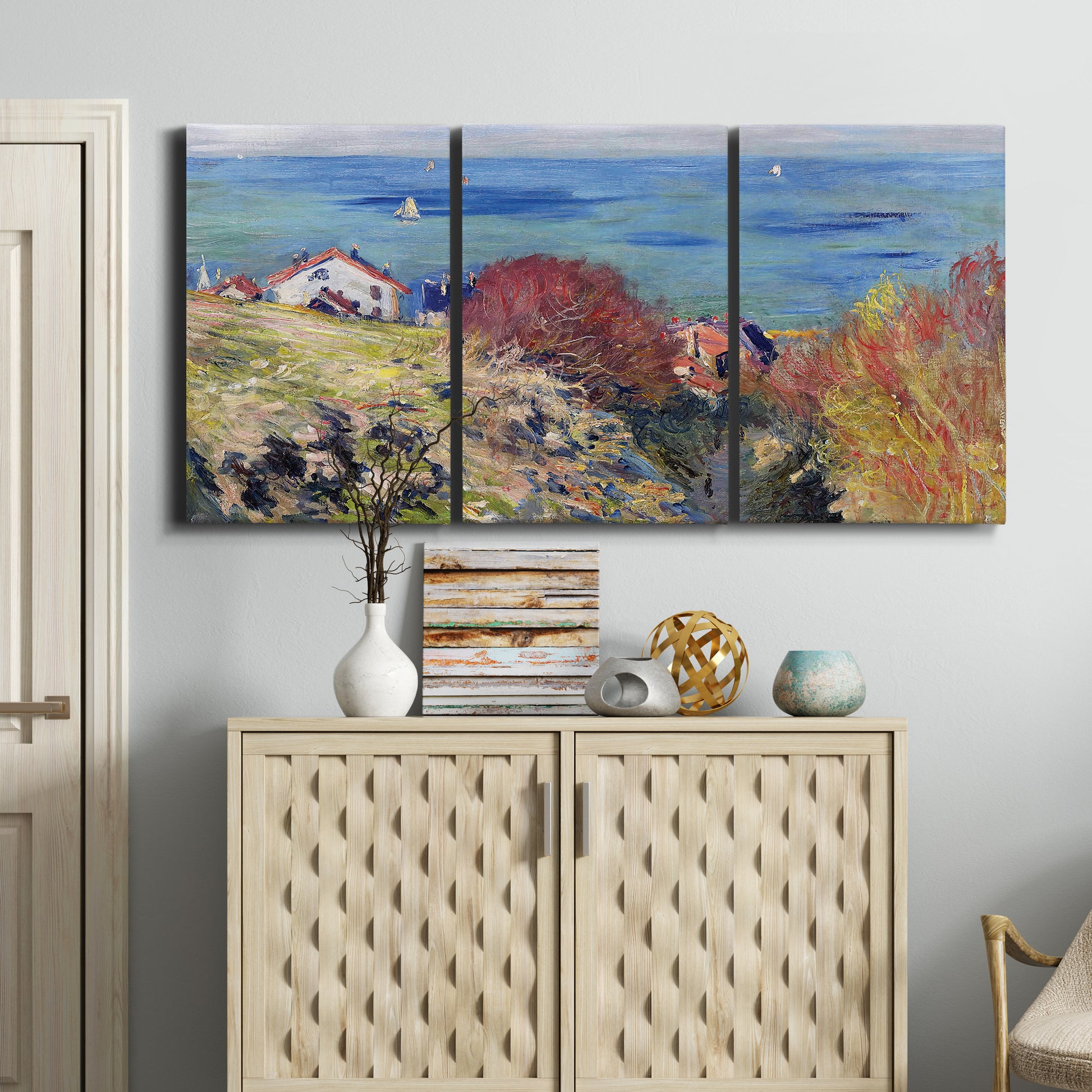 Three-panel canvas wall art featuring coastal village shoreline landscape, displayed above a cabinet in an entryway.
