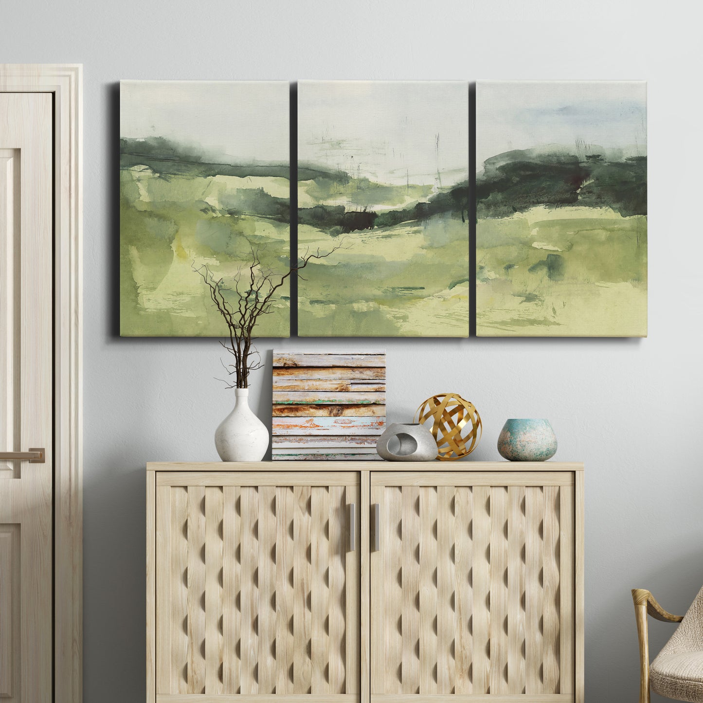 Three-panel canvas wall art featuring rolling hillside countryside landscape, displayed above a cabinet in an entryway.