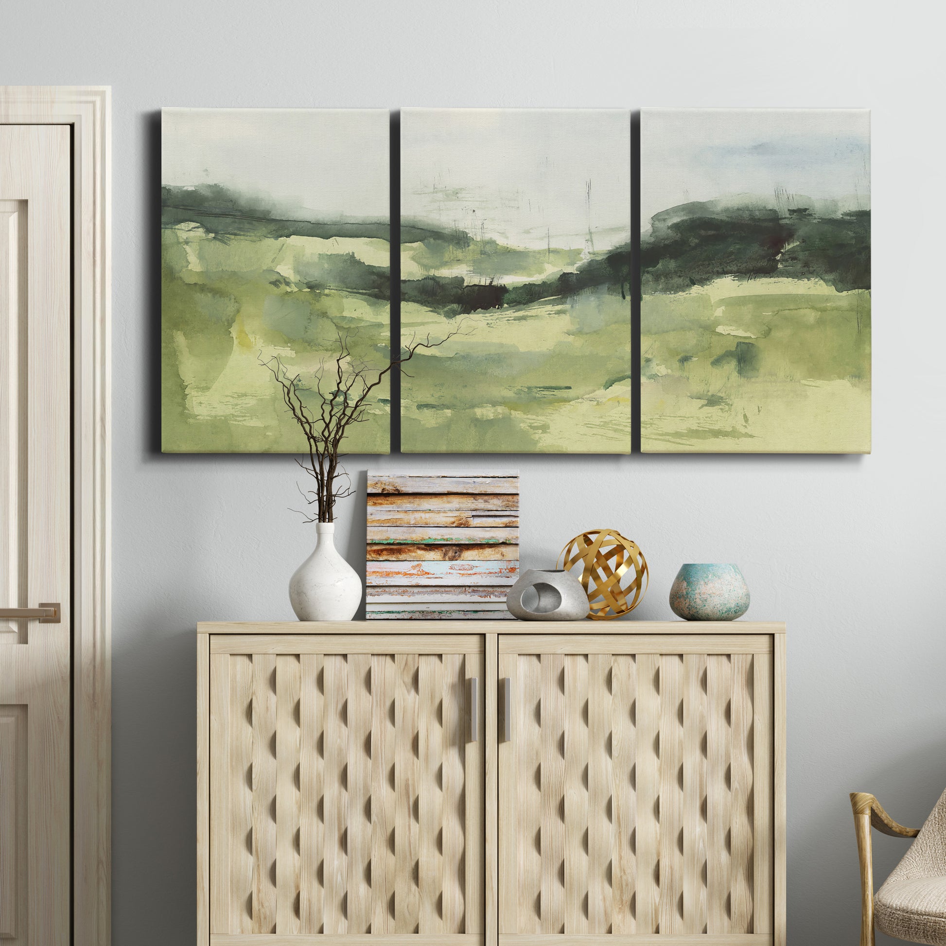 Three-panel canvas wall art featuring rolling hillside countryside landscape, displayed above a cabinet in an entryway.