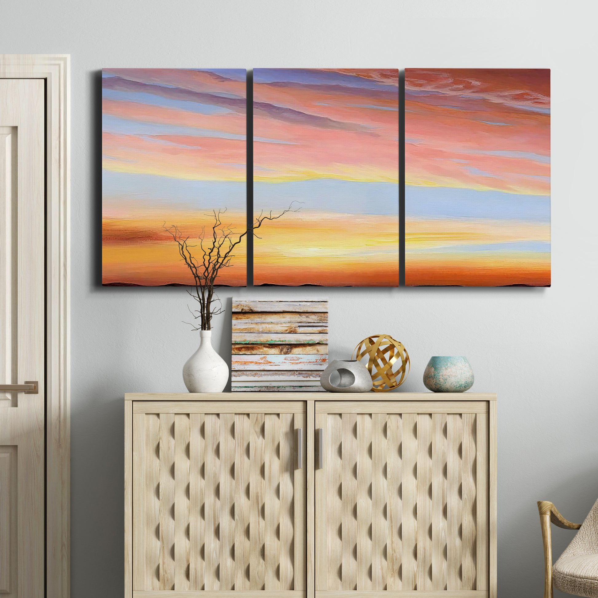 Three-panel canvas wall art featuring glowing sunset sky over landscape, displayed above a cabinet in an entryway.
