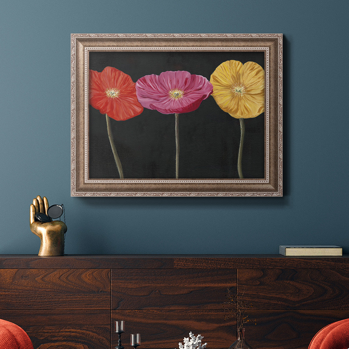 Contemporary poppy flower artwork in an ornate traditional silver frame displayed in a dark-toned interior setting.