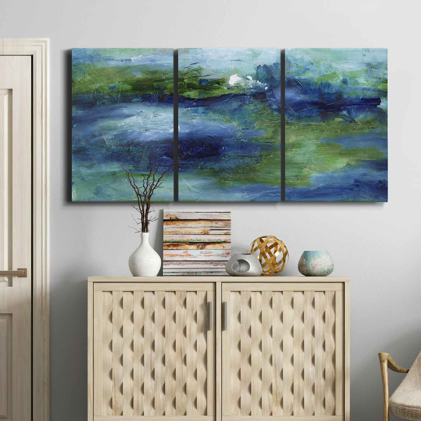 Three-panel canvas wall art featuring flowing blue abstract watercolor, displayed above a cabinet in an entryway.