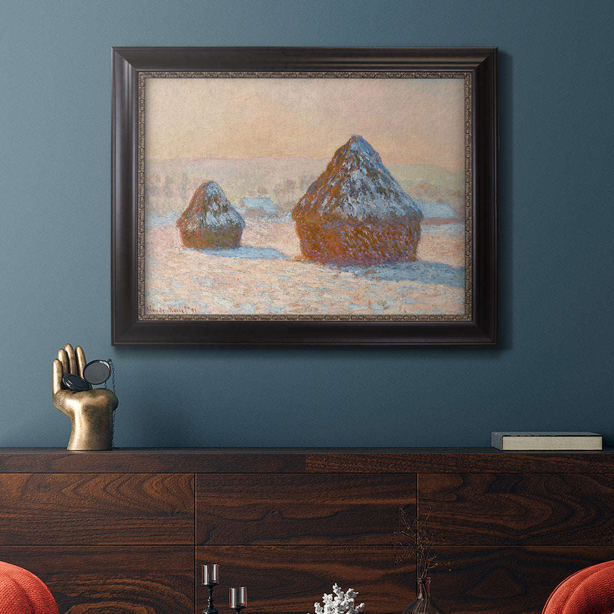 Impressionist winter haystack scene by Claude Monet in an ornate black frame with gilded inner detail displayed in a dark-toned interior setting.