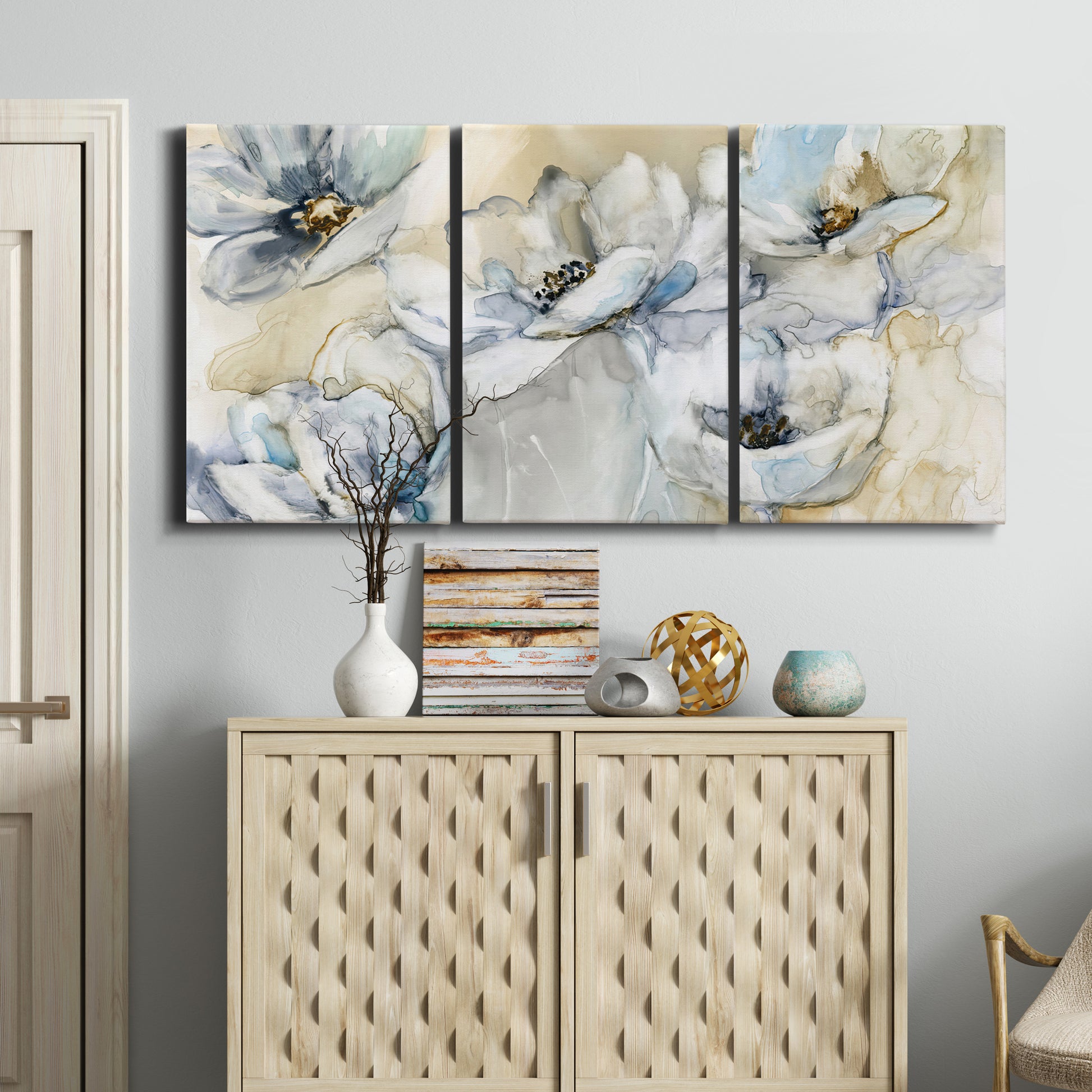 Three-panel canvas wall art featuring delicate watercolor floral blooms, displayed above a cabinet in an entryway.
