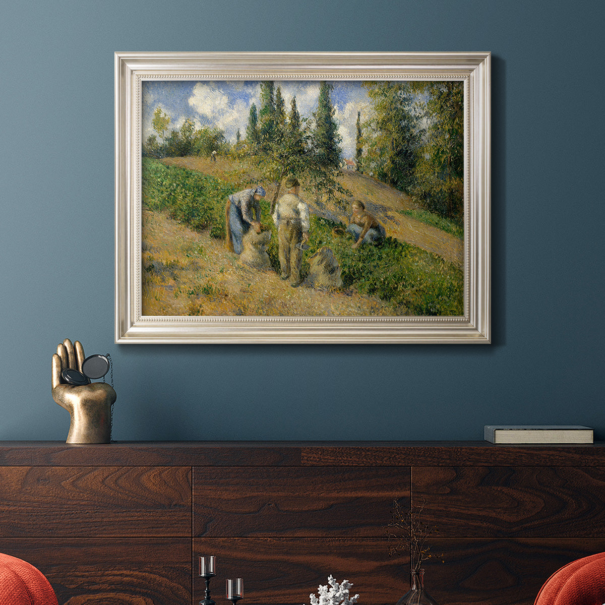 Impressionist countryside harvest scene by Camille Pissarro in an ornate champagne frame displayed in a dark-toned interior setting.