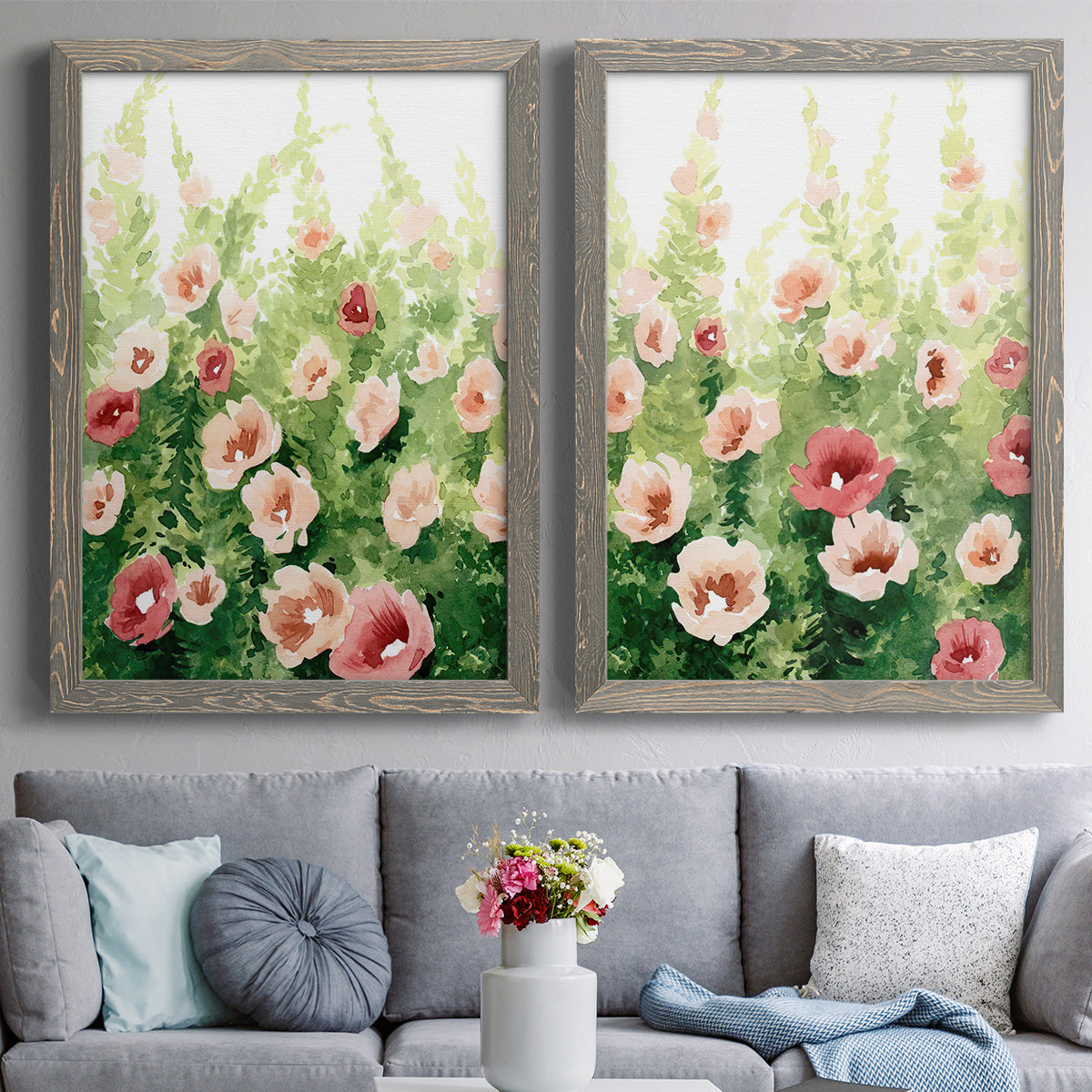 Set of two gray barnwood framed canvas prints depicting paired luminous impressionistic floral paintings with loose blossoms, green stems, and sunlit watercolor texture above a sofa in a contemporary living room.