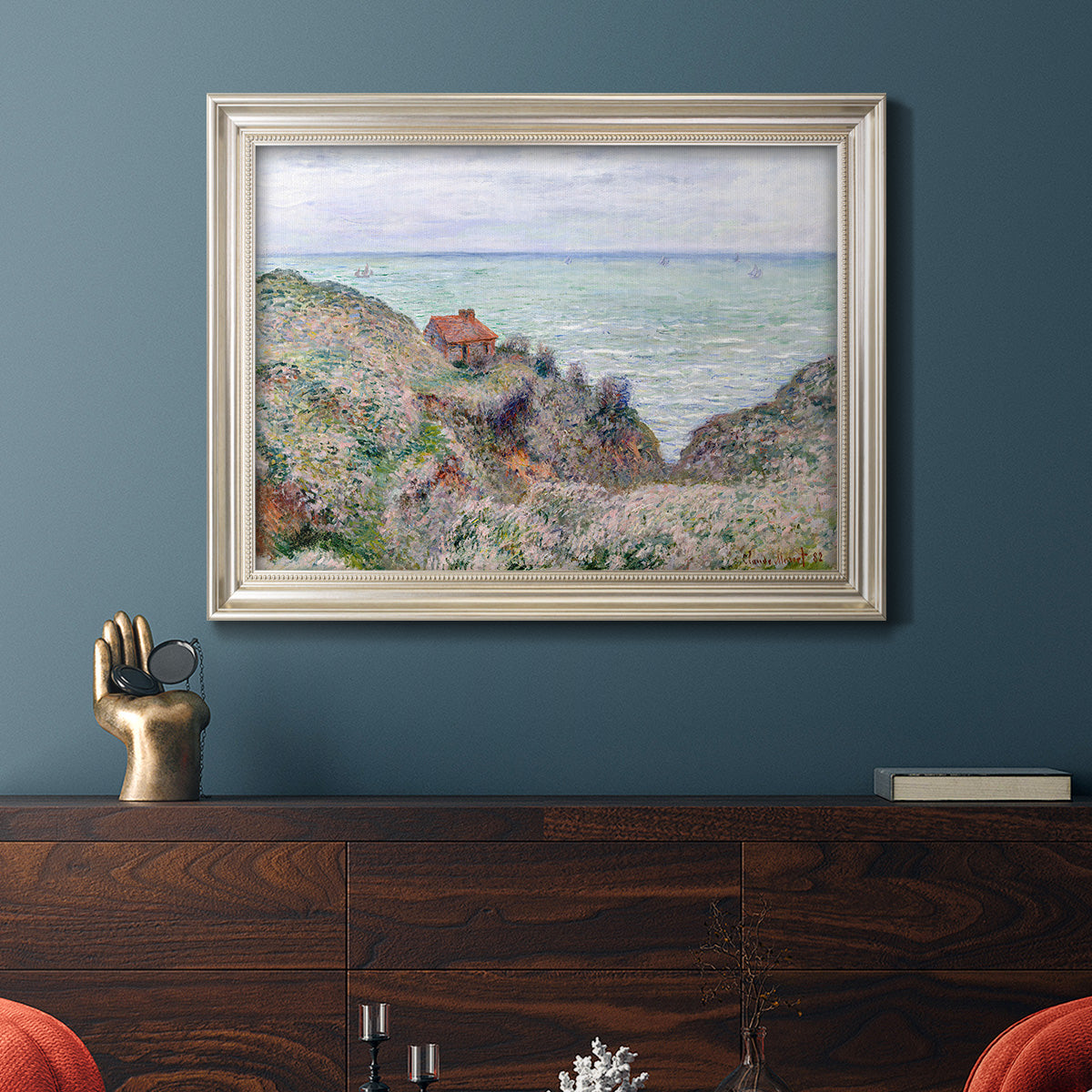 Impressionist coastal watch cabin scene by Claude Monet in an ornate champagne frame displayed in a dark-toned interior setting.