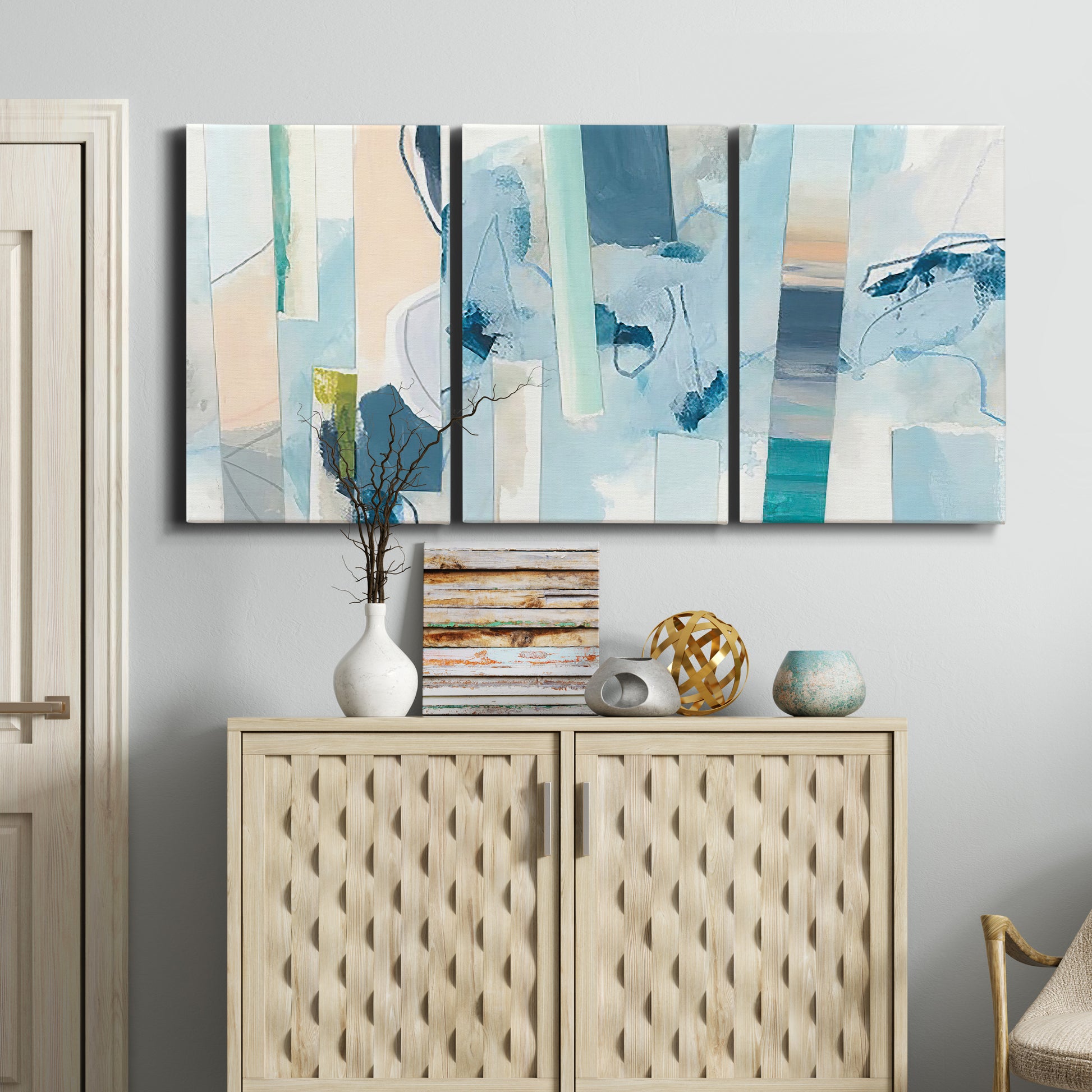 Three-panel canvas wall art featuring layered geometric abstract strata forms, displayed above a cabinet in an entryway.
