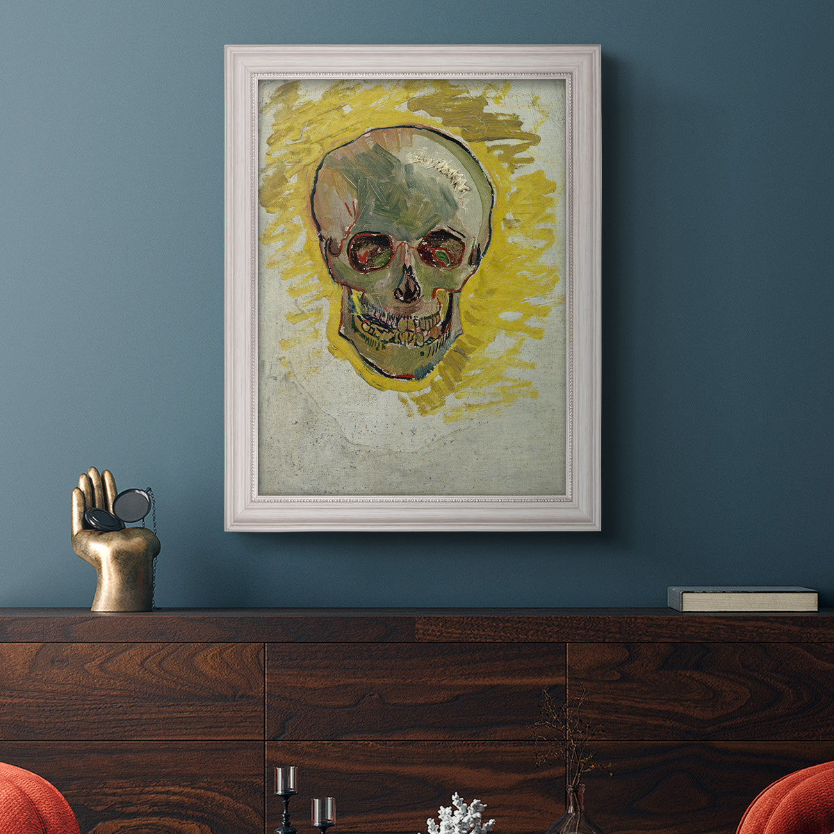 Expressive skull study painting by Vincent van Gogh in an ornate weathered white frame displayed in a dark-toned interior setting.