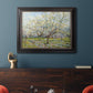 Impressionist white-blossomed orchard landscape by Vincent van Gogh in an ornate black frame with gilded inner detail displayed in a dark-toned interior setting.