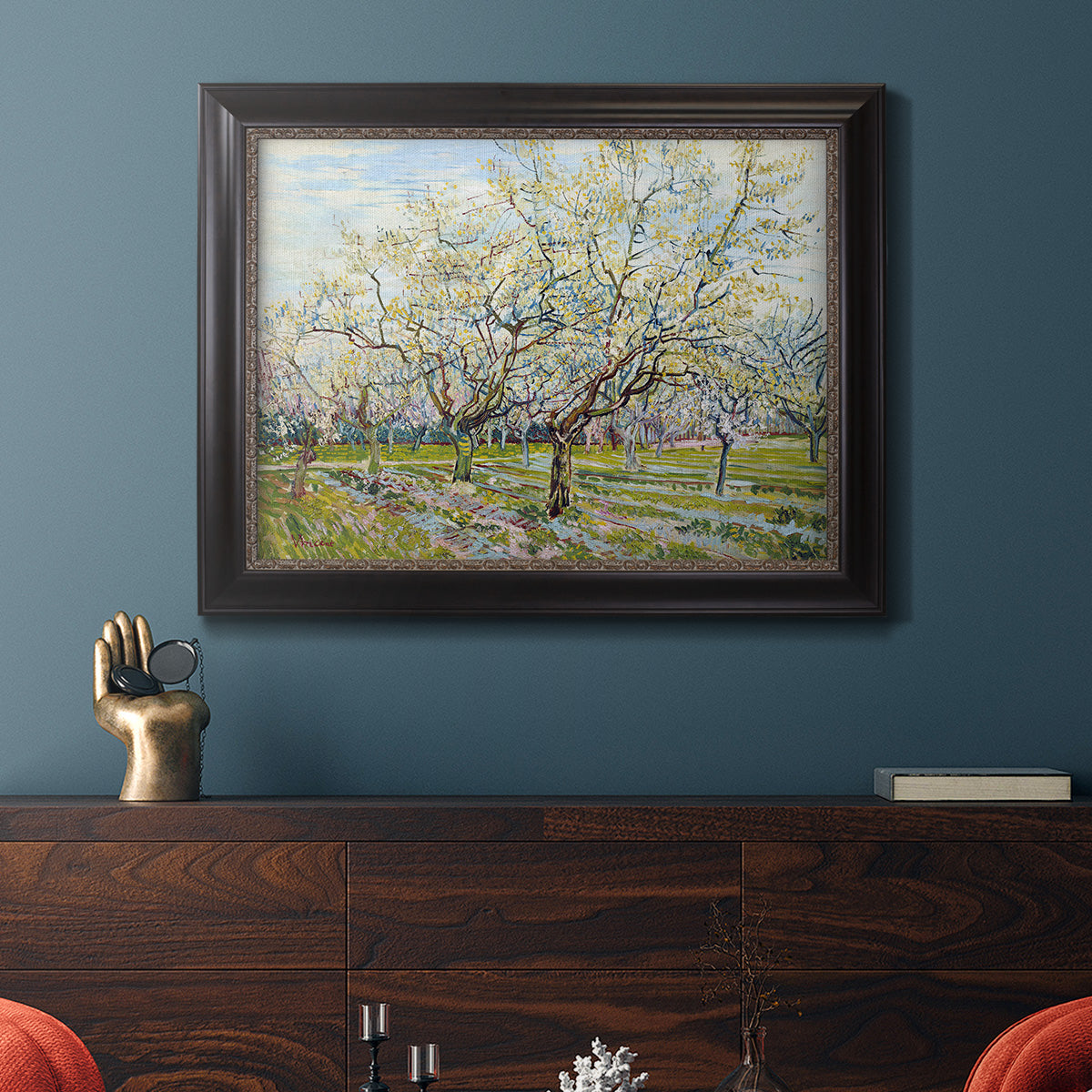 Impressionist white-blossomed orchard landscape by Vincent van Gogh in an ornate black frame with gilded inner detail displayed in a dark-toned interior setting.