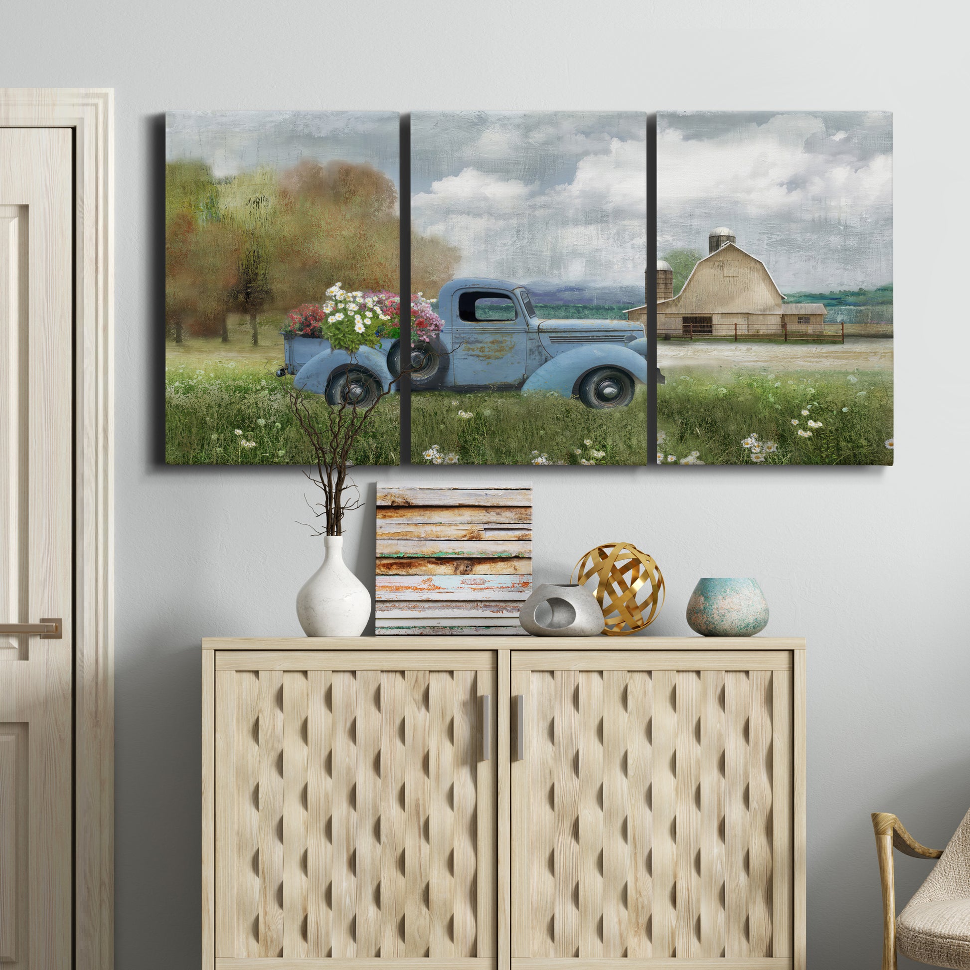 Three-panel canvas wall art featuring vintage blue truck with flower load, displayed above a cabinet in an entryway.