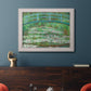 Impressionist garden scene with Japanese bridge and water lilies by Claude Monet in an ornate weathered white frame displayed in a dark-toned interior setting.