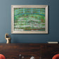 Impressionist garden scene with Japanese bridge and water lilies by Claude Monet in an ornate champagne frame displayed in a dark-toned interior setting.